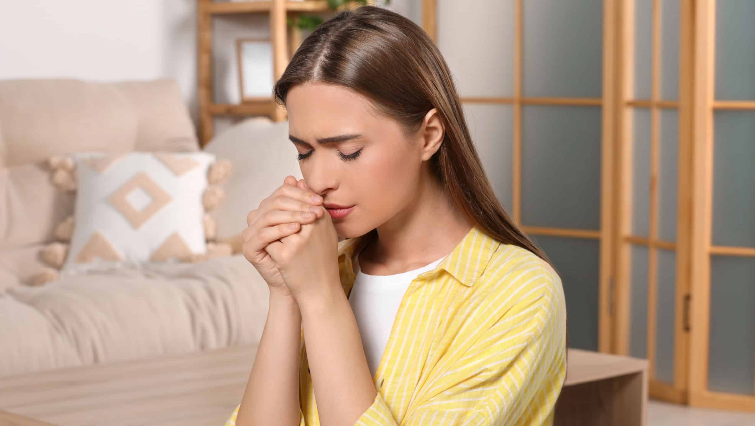 Woman with clasped hands praying at home