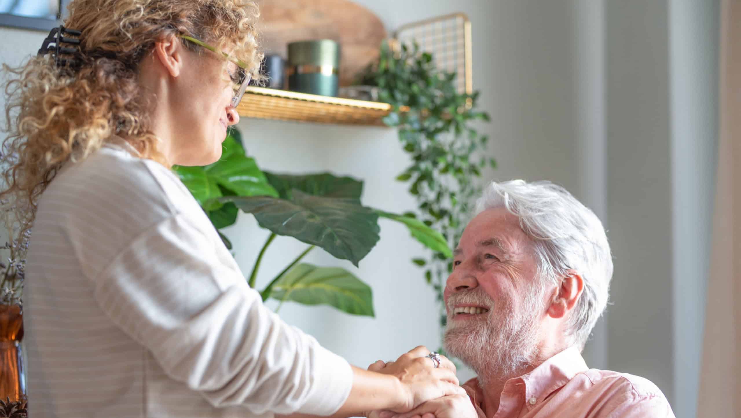 Portrait of middle aged woman lovingly caring for her old retired father at home while spending time together, support and care for our elders