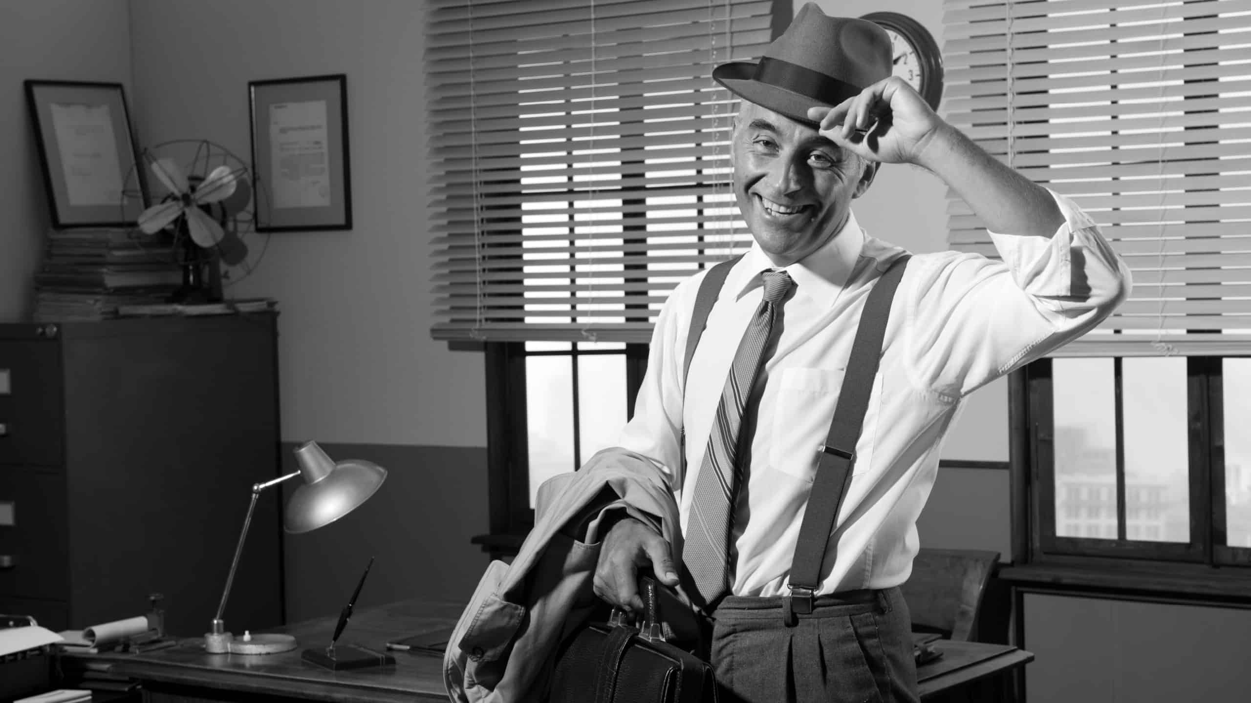 Smiling businessman leaving office holding briefcase and trench coat, 1950s style.