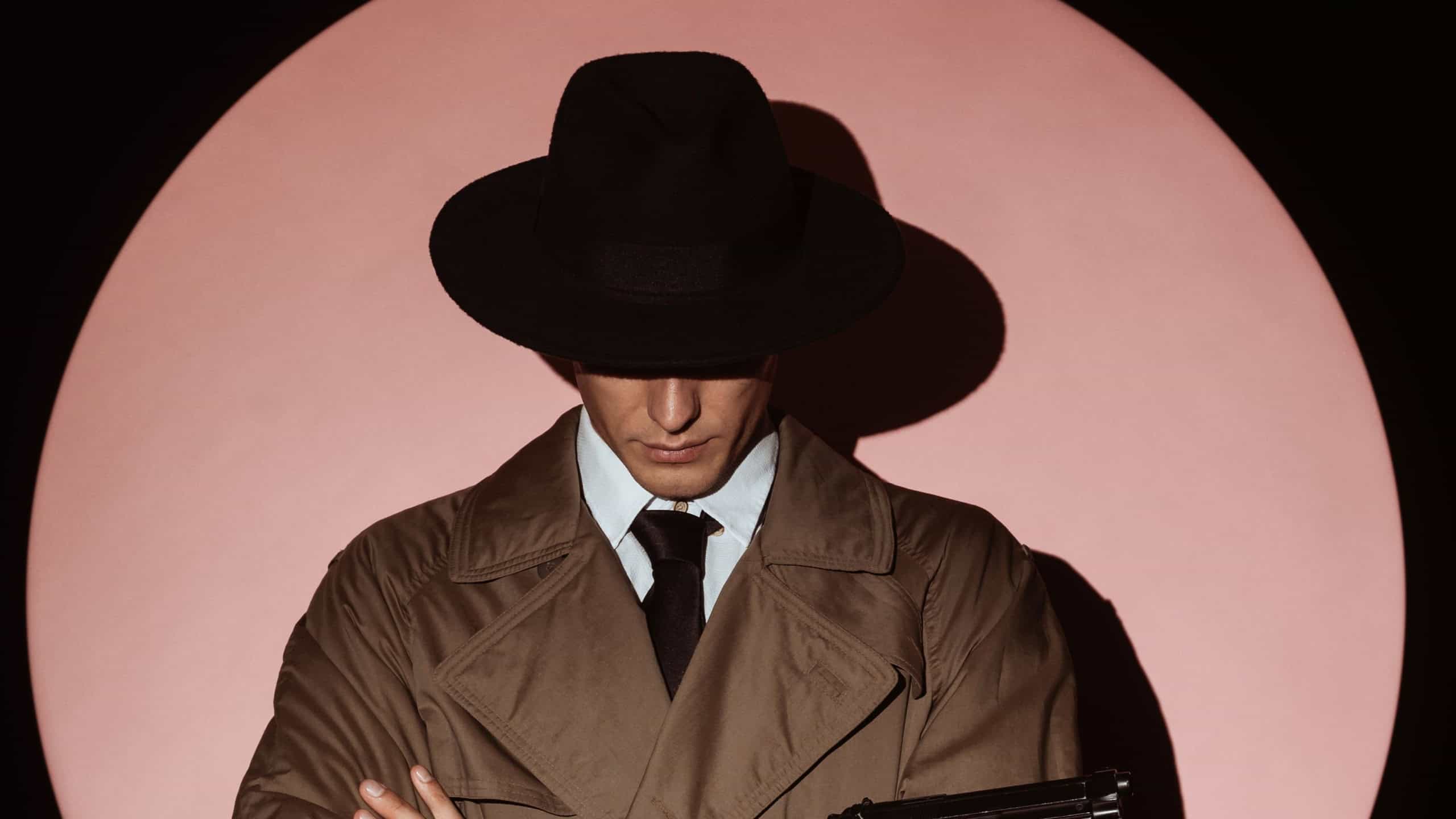 Portrait of a male detective in a coat and hat with a gun in his hands. Dramatic portrait-silhouette in the style of detective films and spy books of the 1950s. The silhouette of a spy in a circle