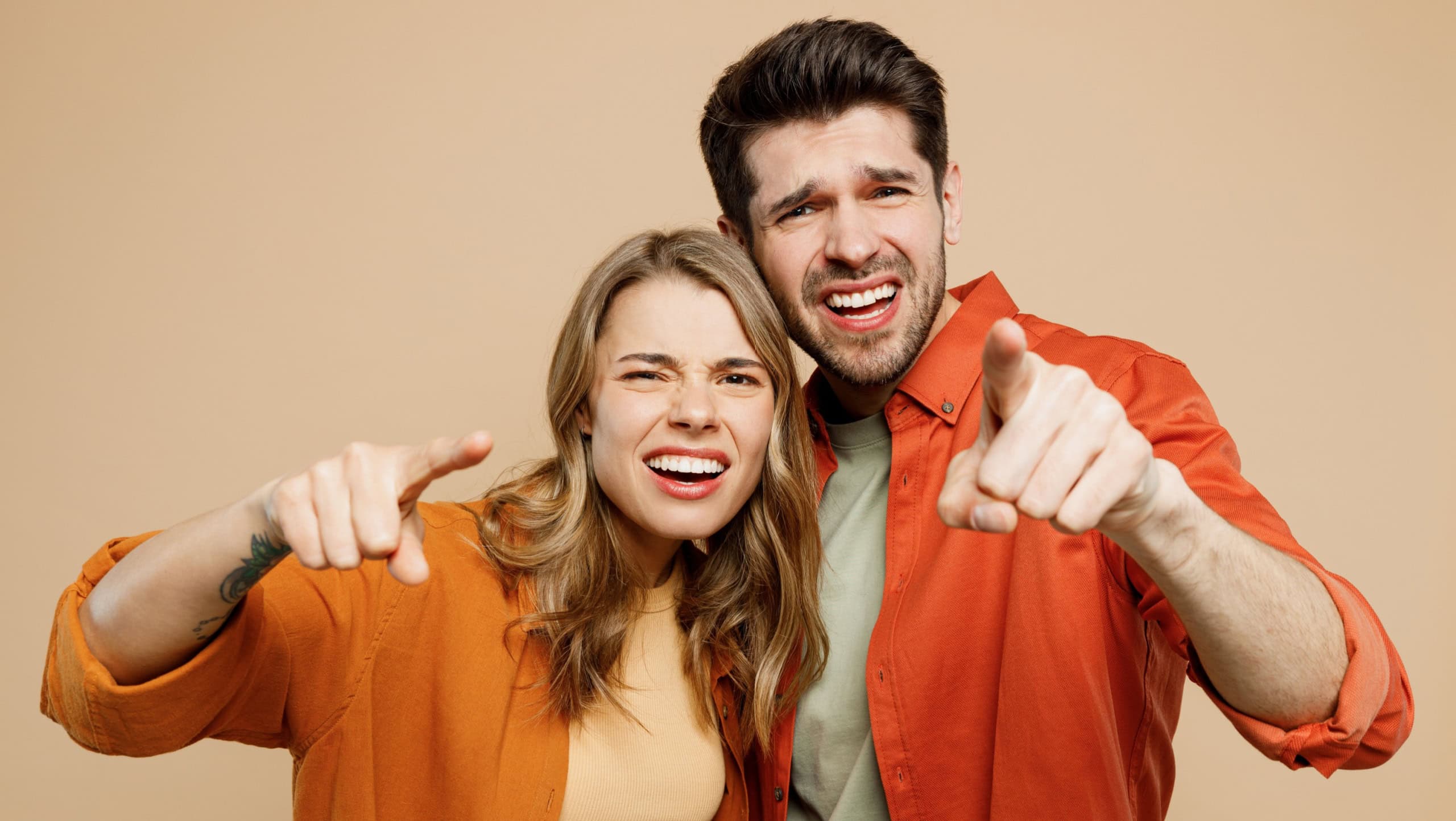 Young sad disappointed couple two friends family man woman wear casual clothes looking camera point index finger on you together isolated on pastel plain light beige color background studio portrait