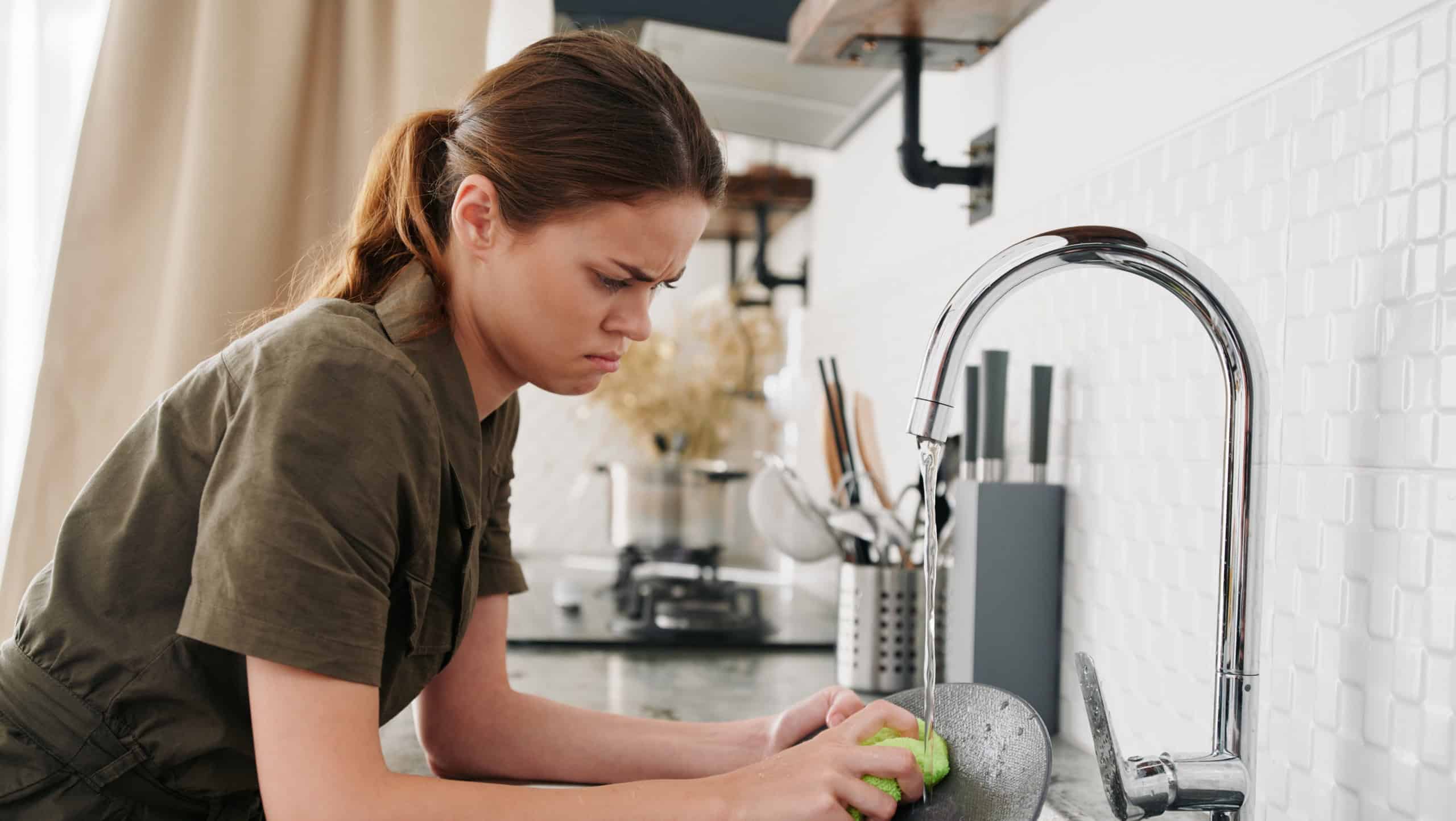 Woman tired and angry hands without gloves washes dishes with a dishwashing sponge with bubbles, household chores, no dishwasher, high water consumption. Stylish kitchen design