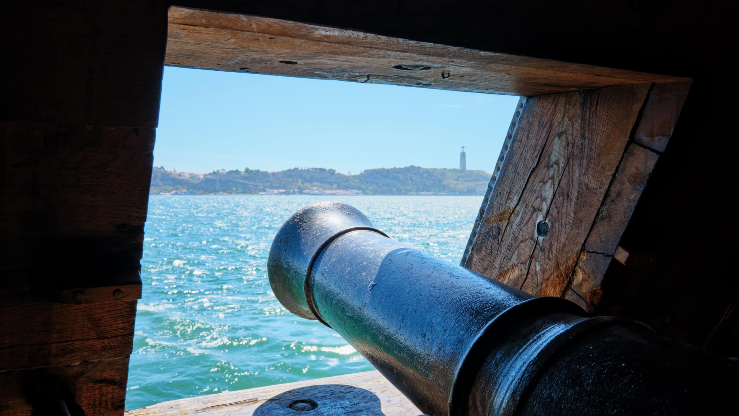 Sea view out of a gunport in hull of the ship over the gun cannon muzzle in on the gun deck of a sailing ship of Age of Sail