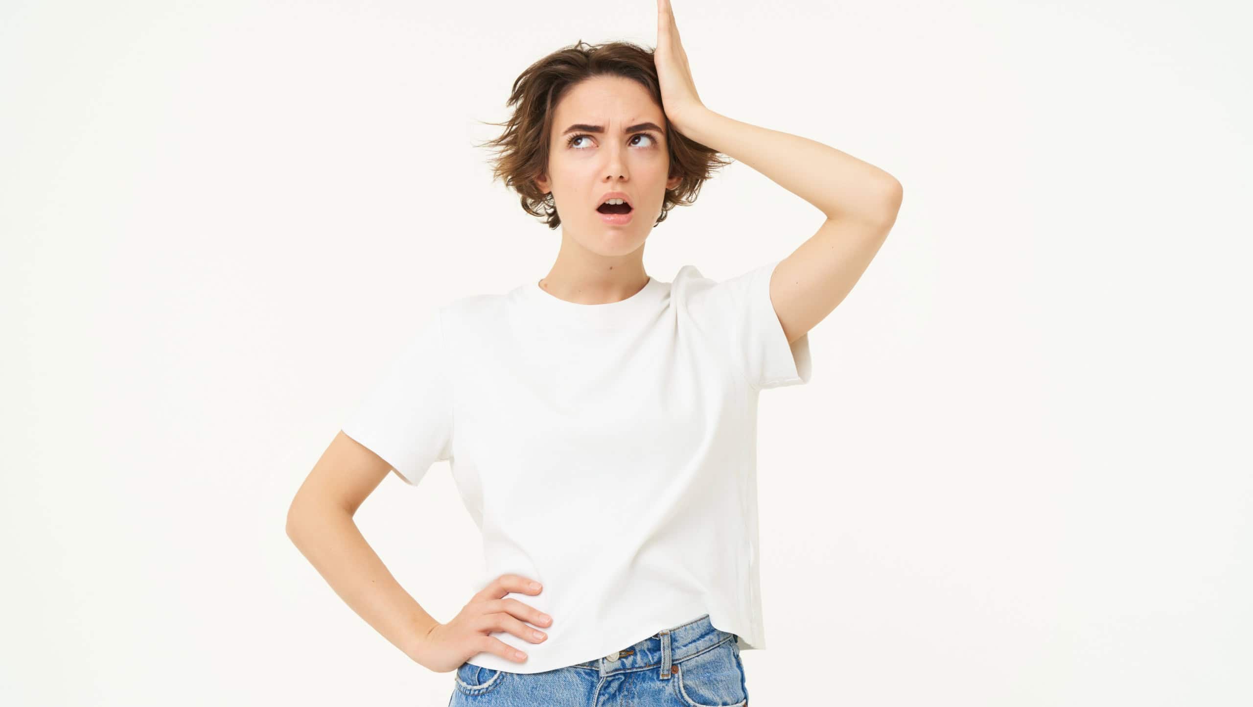 Portrait of forgetful woman, touches her head, remember something important, looks upset or shocked, stands over white background.