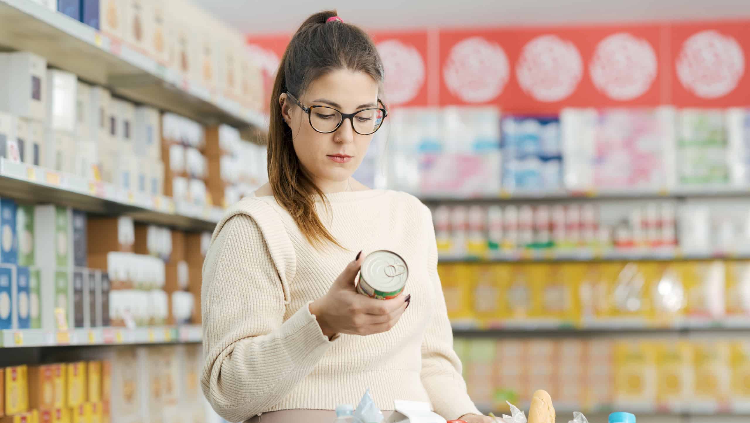 Woman buying groceries at the supermarket, she is holding a can and checking the food label