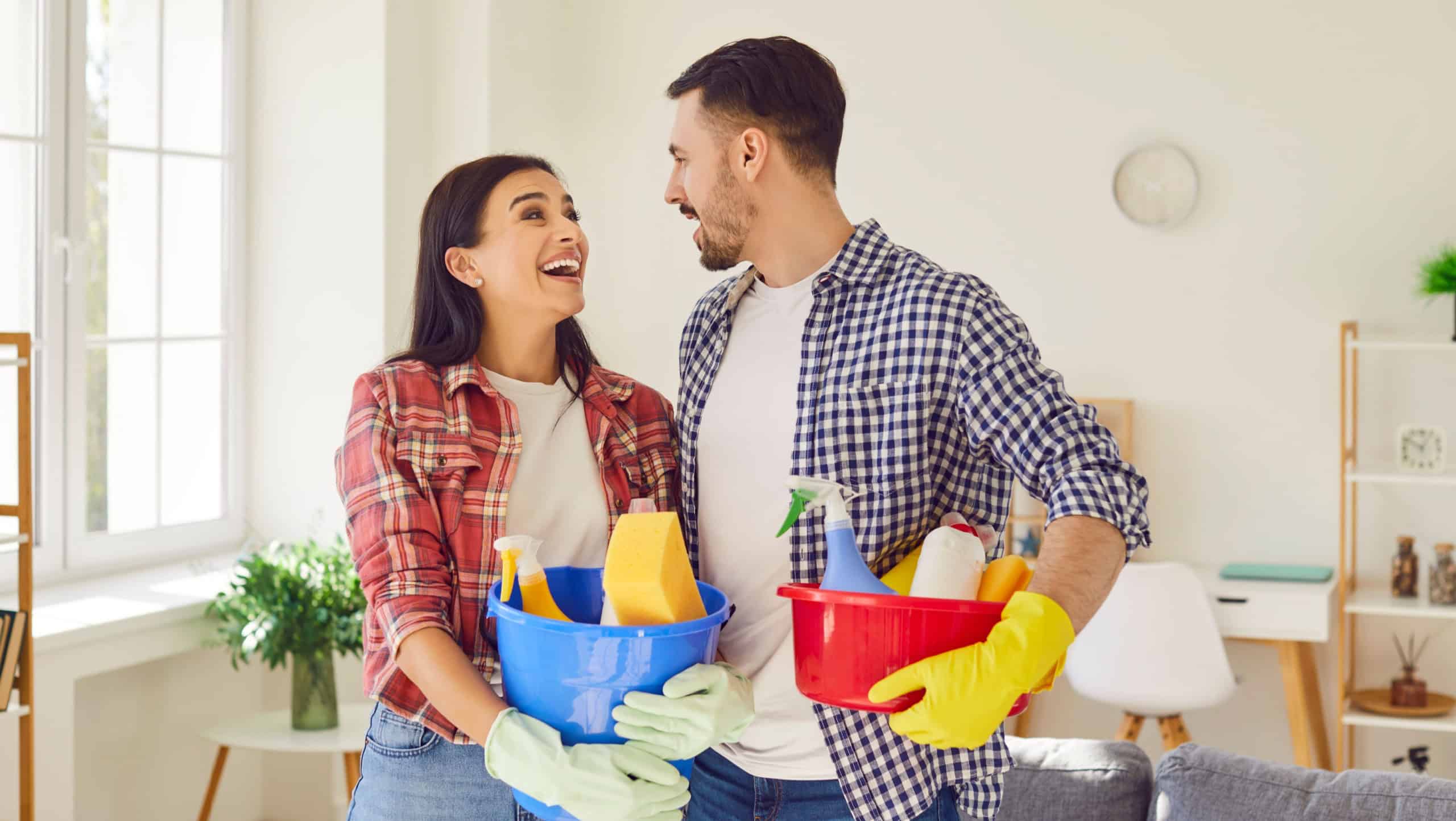 Happy couple, armed with cleaning equipment, bringing joy to the living room. Family showing fun teamwork and shared responsibility, where household chores become moments of connection.