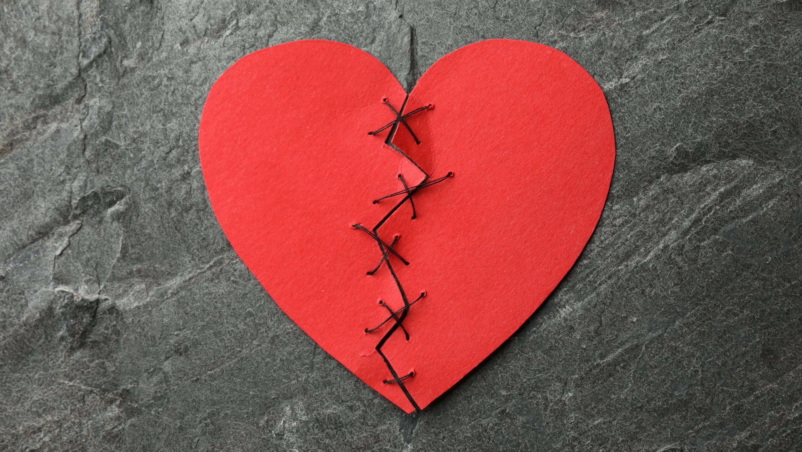 Broken heart. Torn red paper heart sewed with thread on dark grey table, top view
