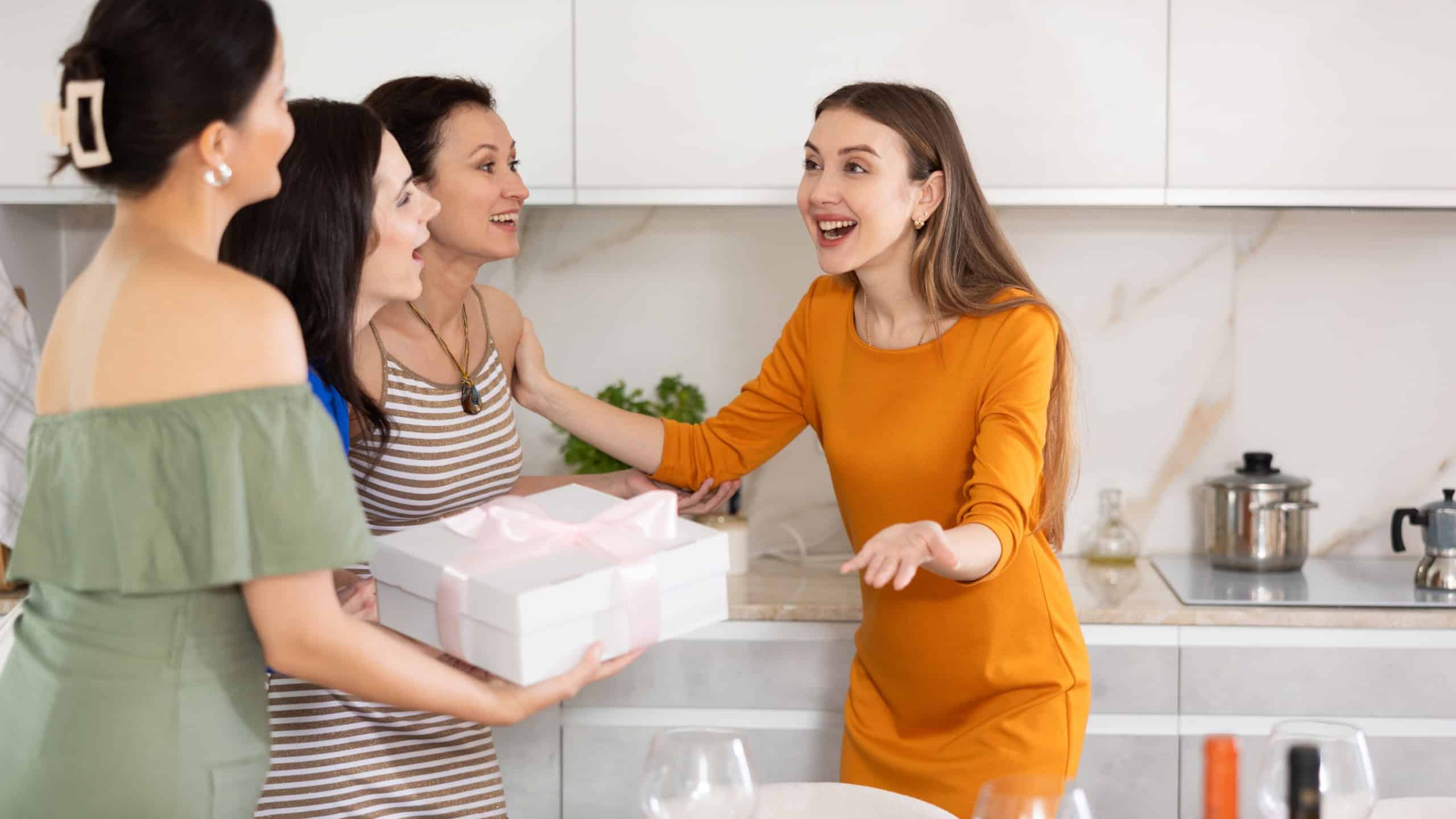 Excited young woman in vibrant festive attire warmly hosting besties bringing unexpected beautifully wrapped gift for friendly home get-together