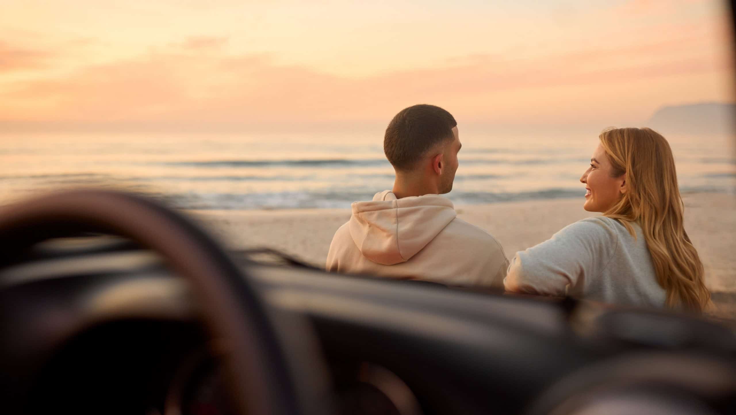 Rear View Of Couple Chatting By Car At Beach Watching Sunrise Together Viewed Through Windshield