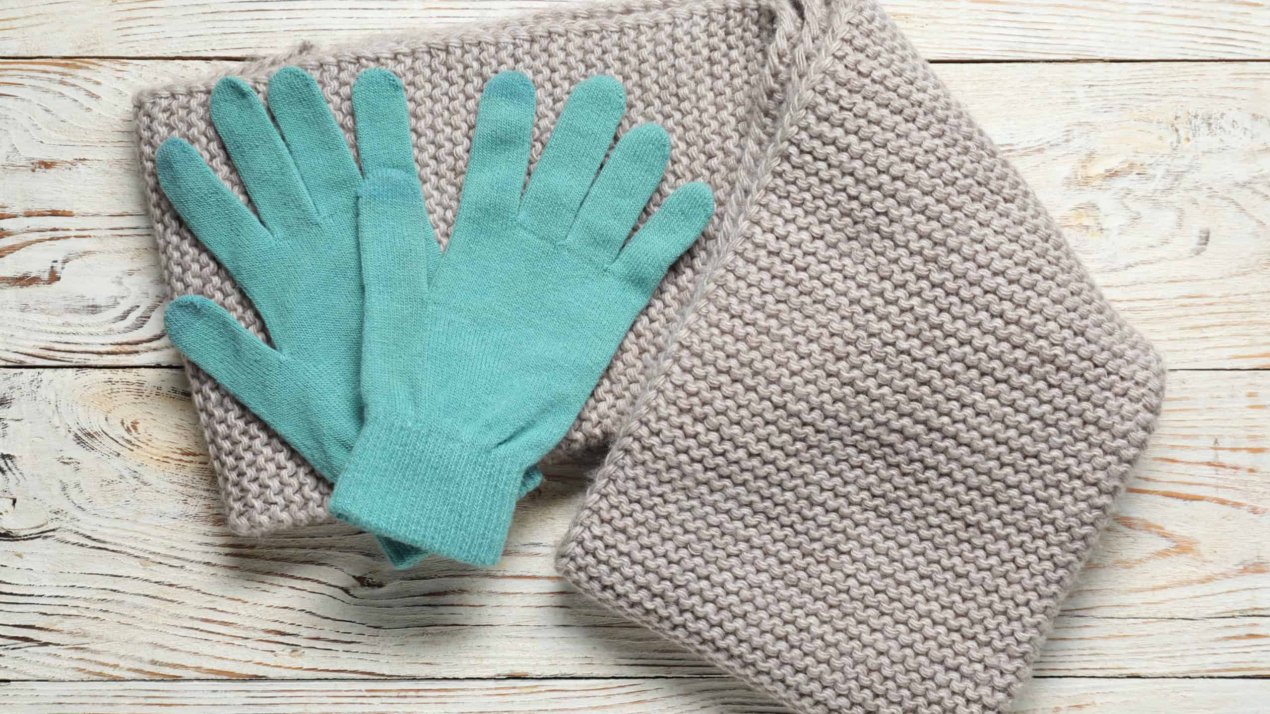Comfortable teal wool gloves with matching knit scarf on rustic wooden background.
