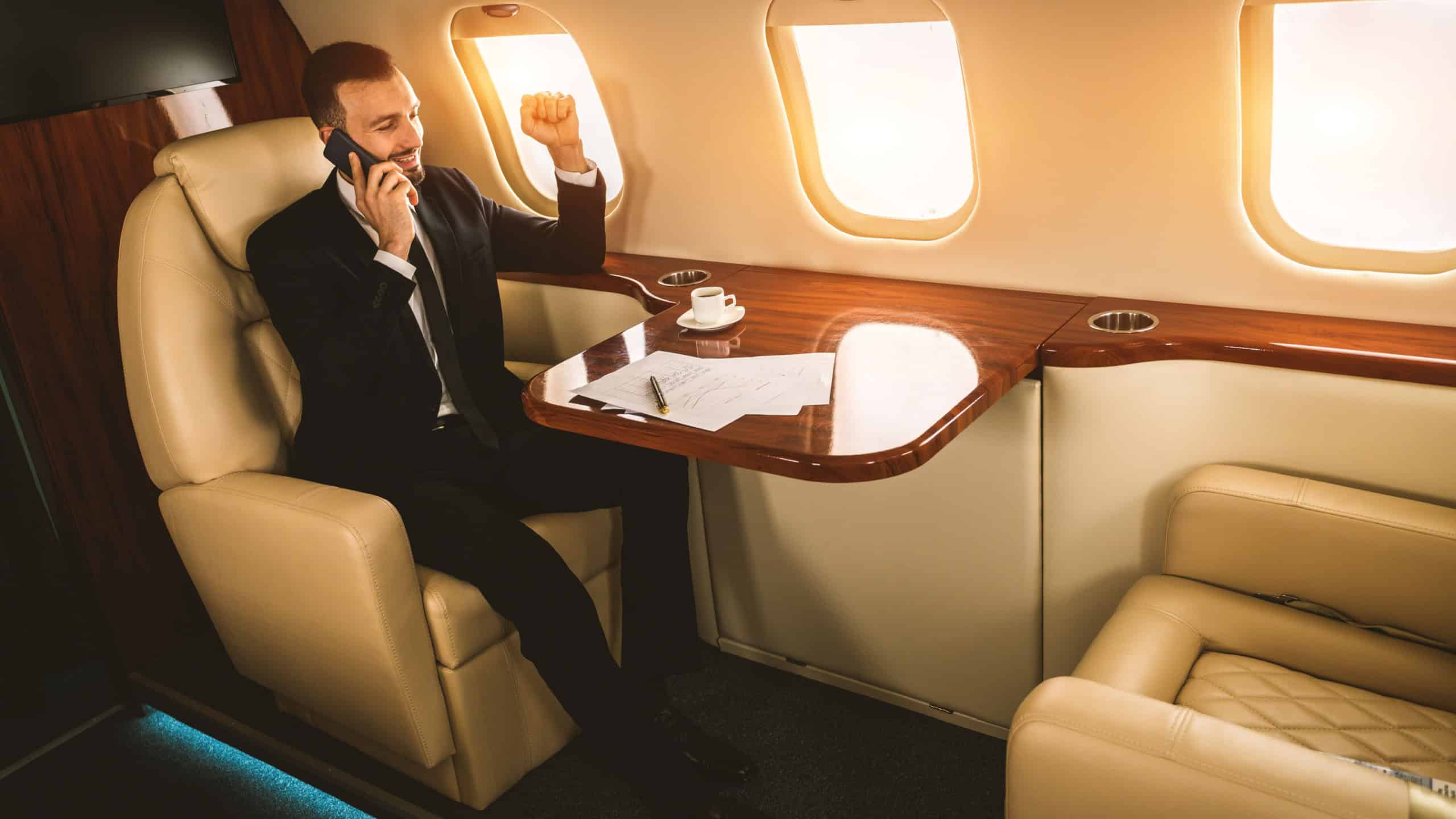 Handsome businessman wearing elegant suit flying on exclusive private jet - Successful entrepreneur sitting in exclusive business class on airplane, concepts about business and trasportation
