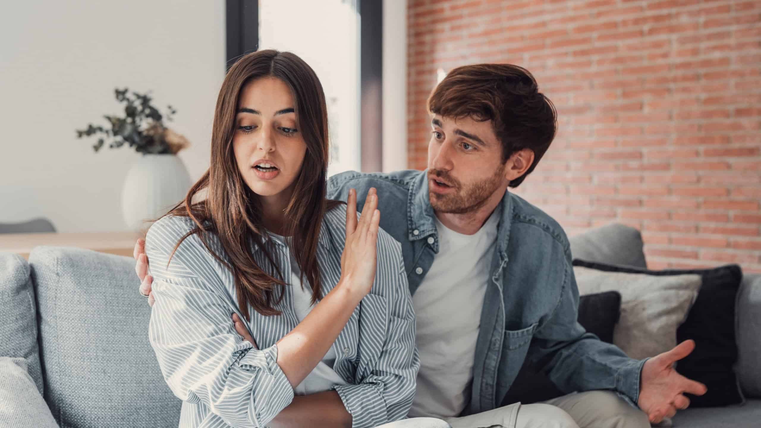 Beautiful lady is depressed, sitting on the couch talking to man, having a dispute with husband or boyfriend, looking desperate and hopeless, having unresolved problem or question