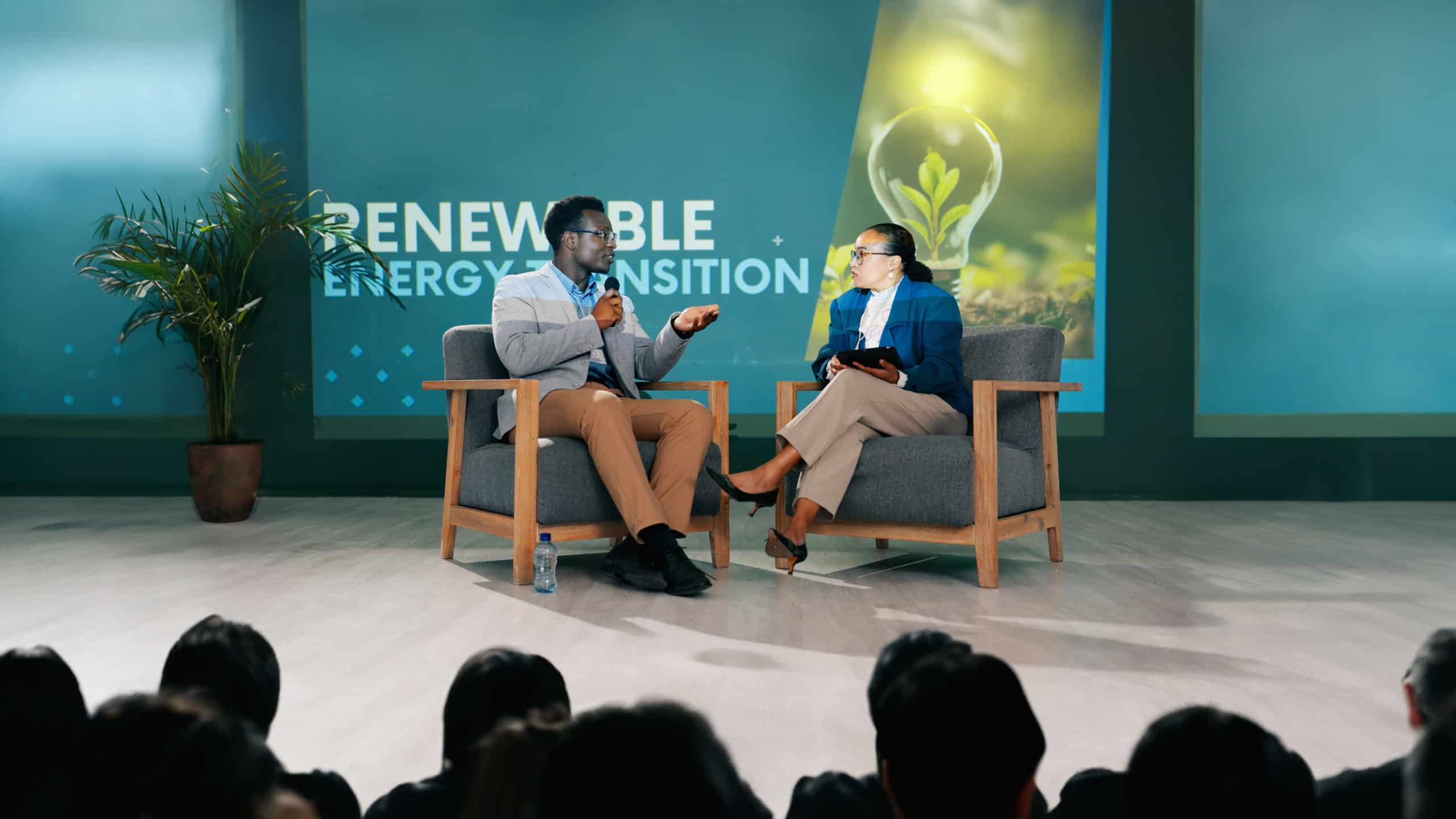 Man, woman and stage for interview at conference for renewable energy, solution and global policy. People, questions and talk in public debate for sustainability, future or plan of action for planet