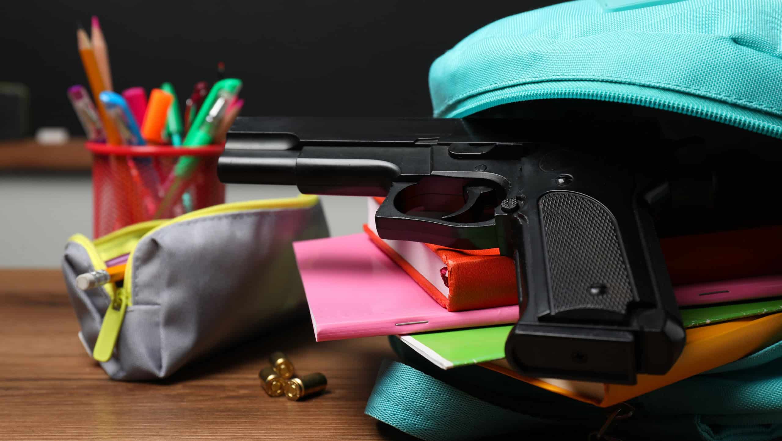 Gun, bullets and school stationery on wooden table near blackboard indoors, closeup