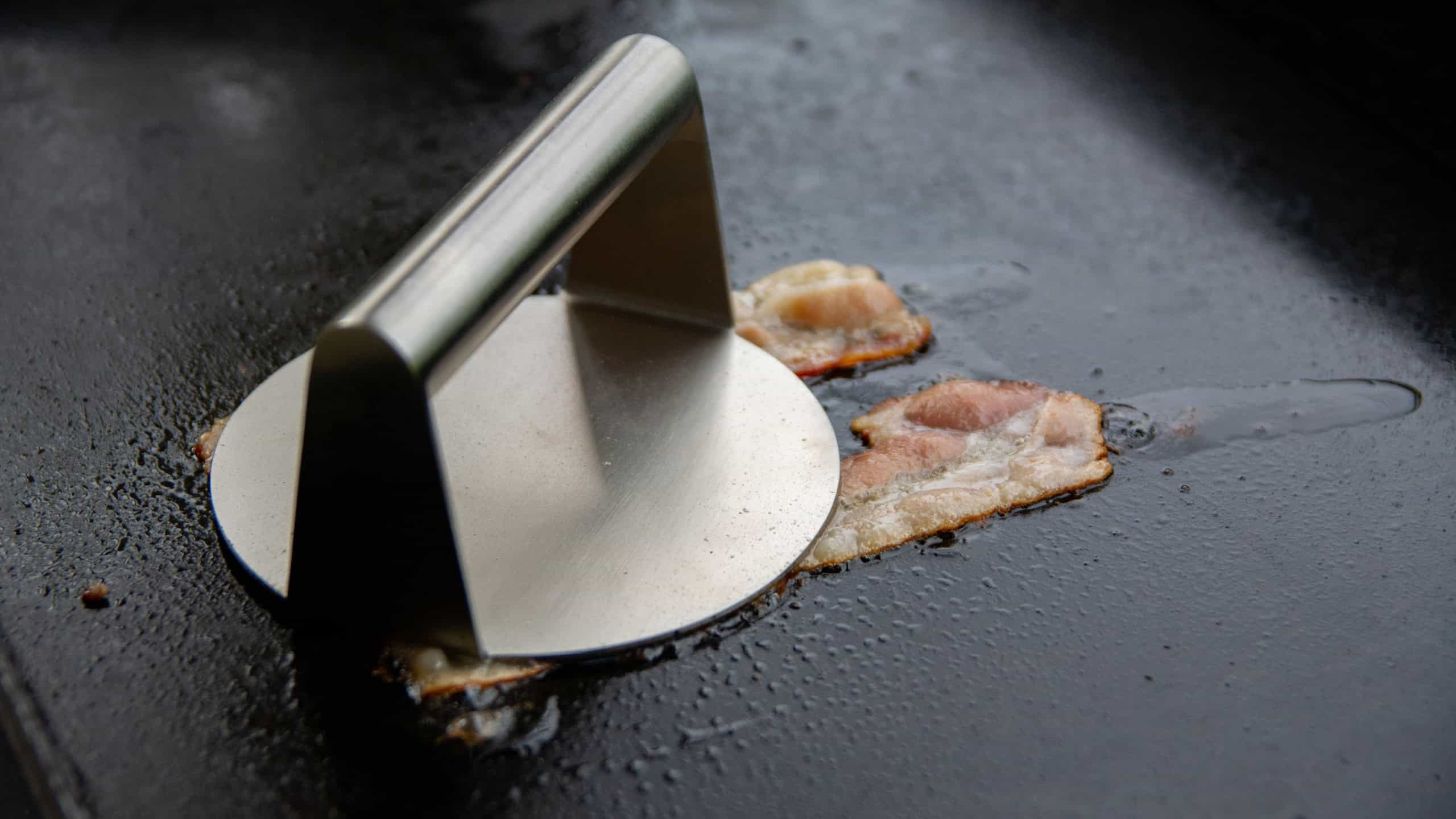 Smasher pressing bacon strips on an electric griddle
