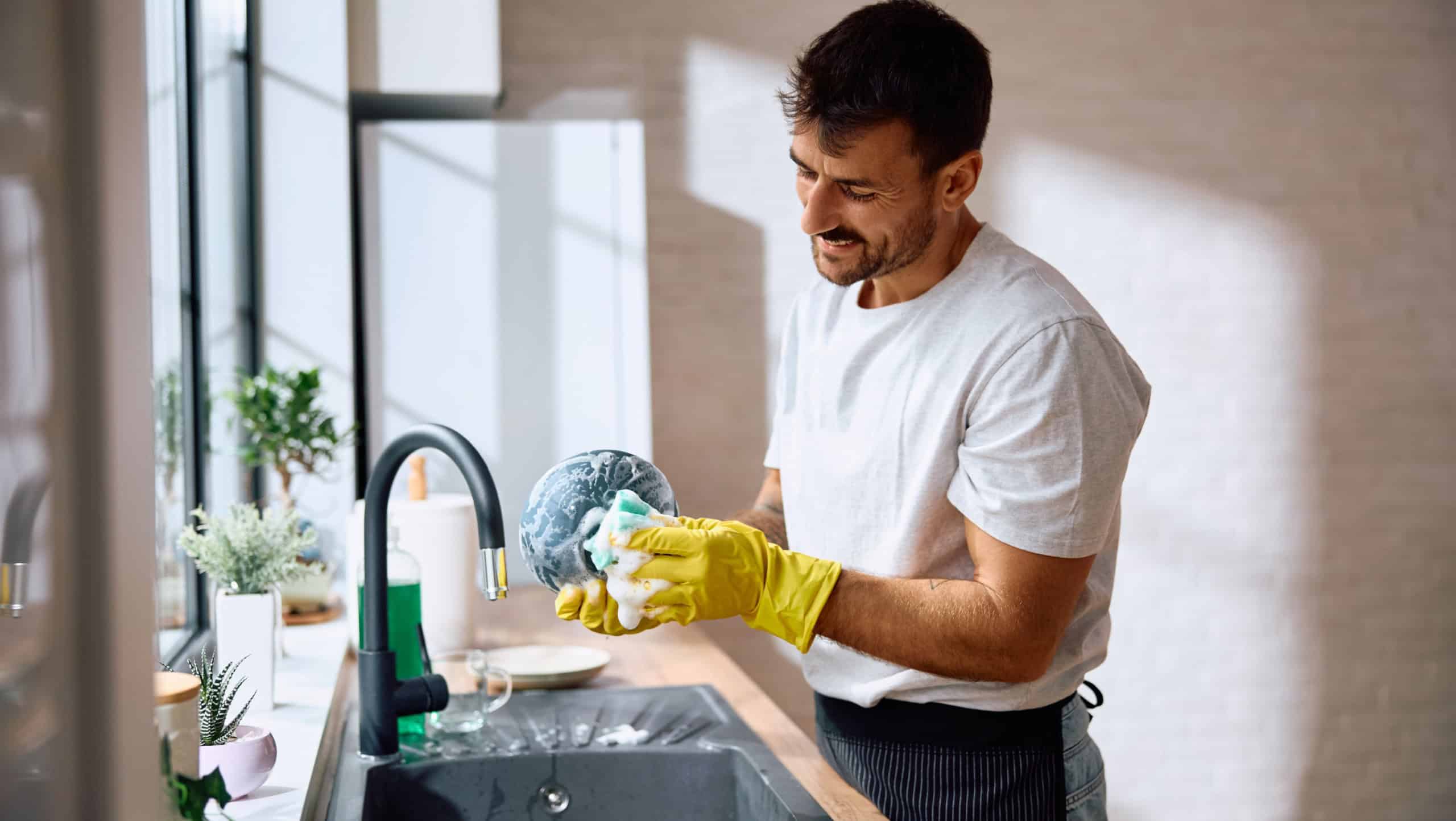 Young smiling man doing dishes in the kitchen. Copy space.