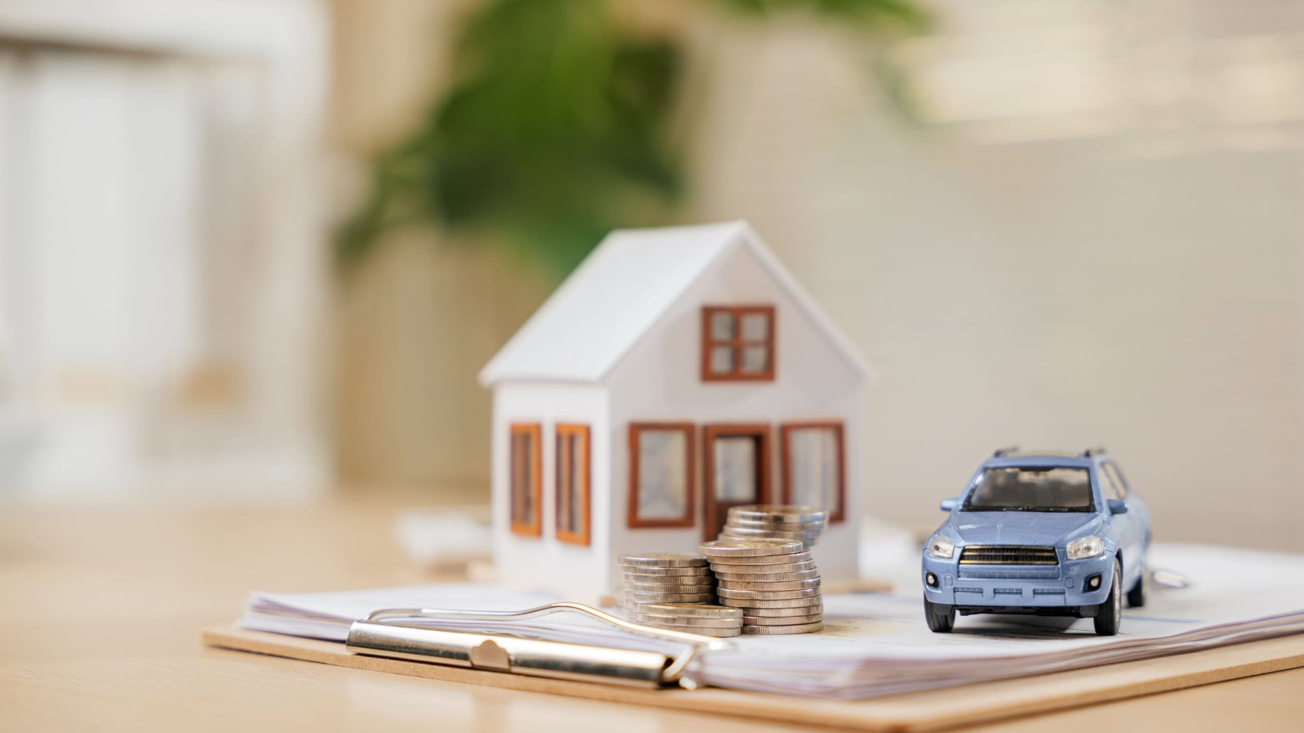 House and car models beside coin stacks on documents highlight real estate and financial planning. A clear representation of banking, savings, and investments for securing future assets.