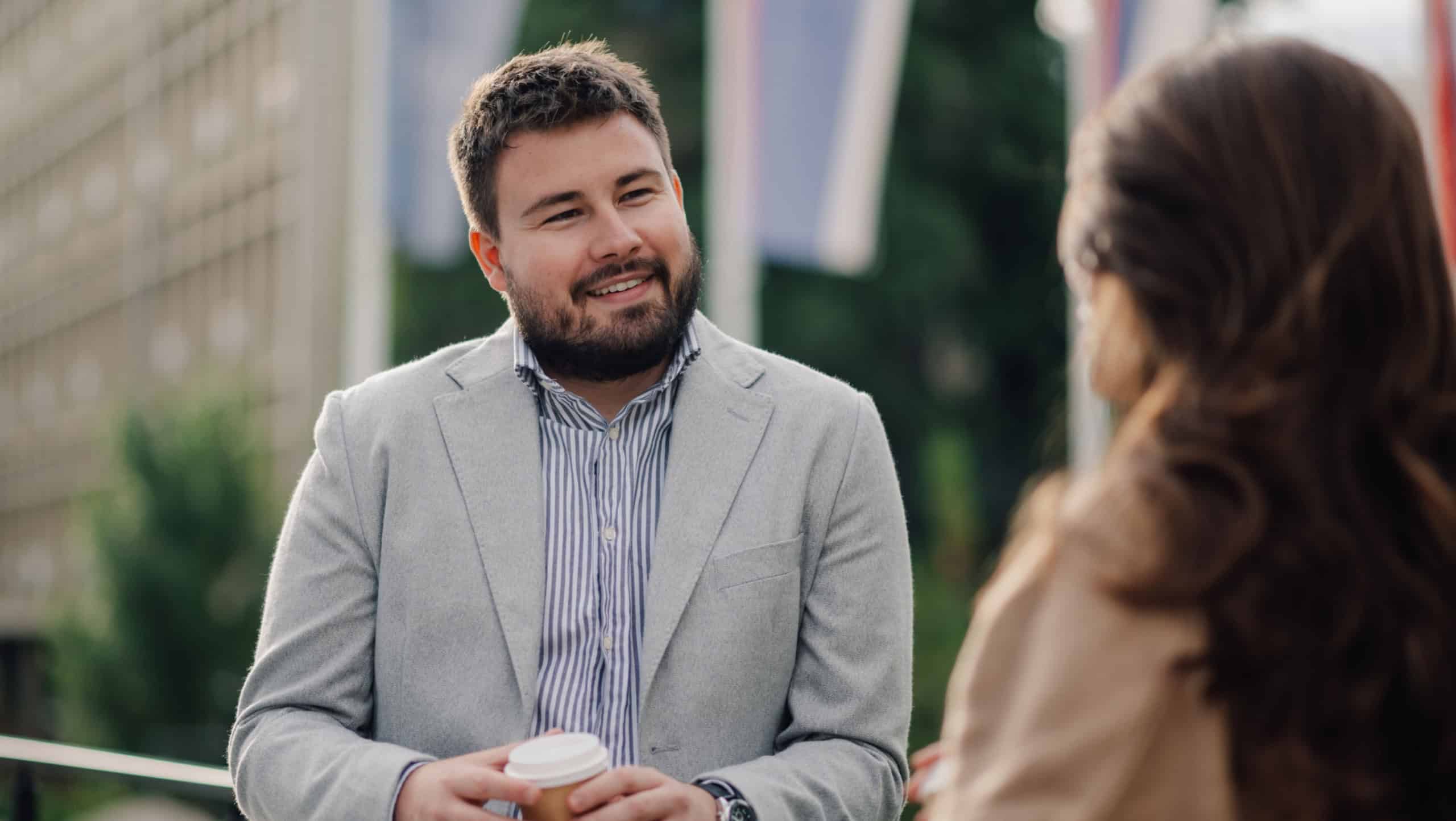 Businessman chats with a female colleague over coffee outside the office, showcasing a modern work life balance in a city setting