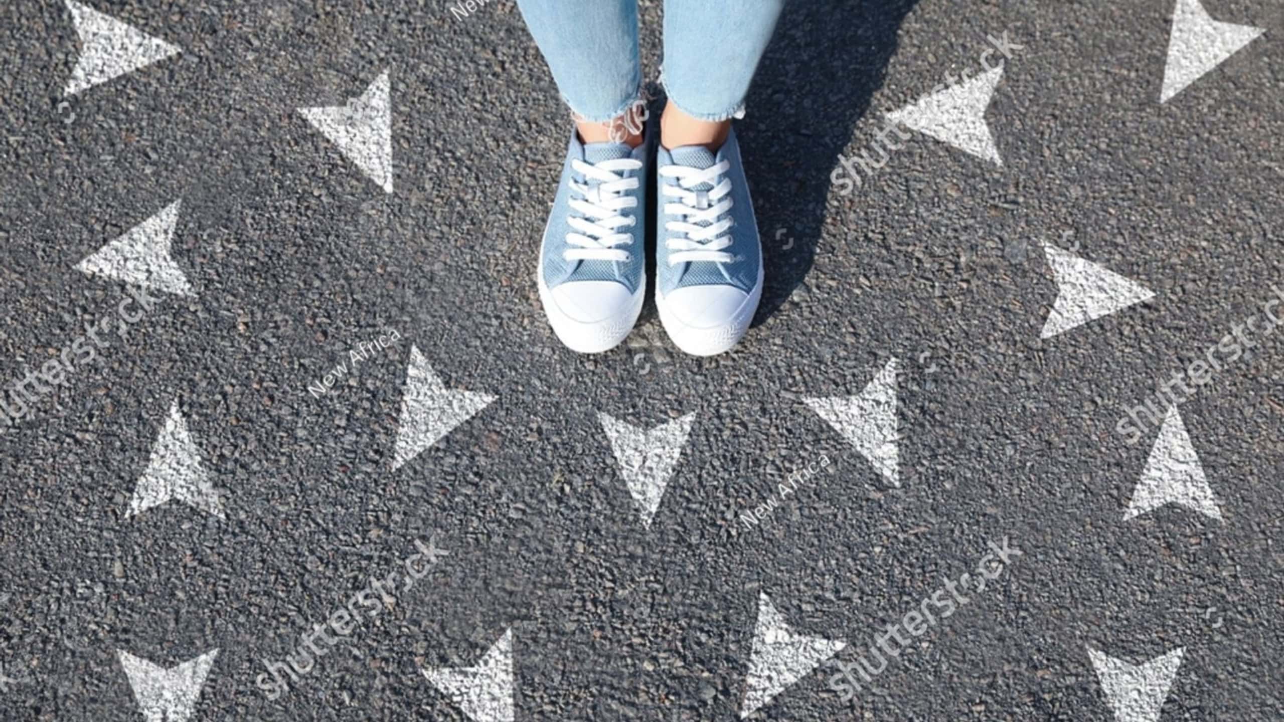 Woman standing near white arrows on asphalt road, closeup. Concepts of choice, decision, different way, alternative