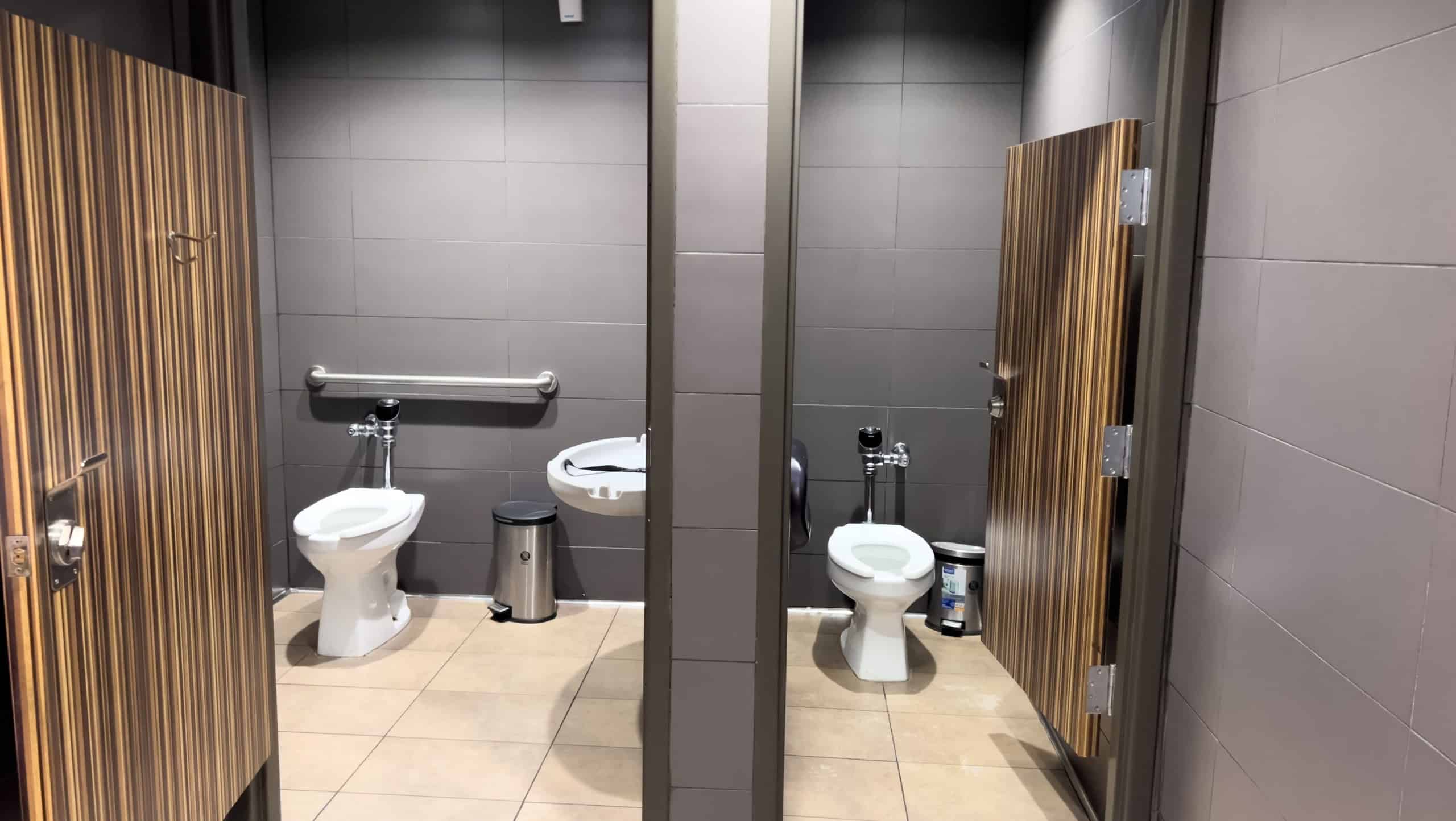 Broomfield, Colorado, USA-January 26, 2025-A clean public restroom featuring two stalls with white toilets and gray tiled walls The restroom is equipped with stainless steel grab bars and toilet paper