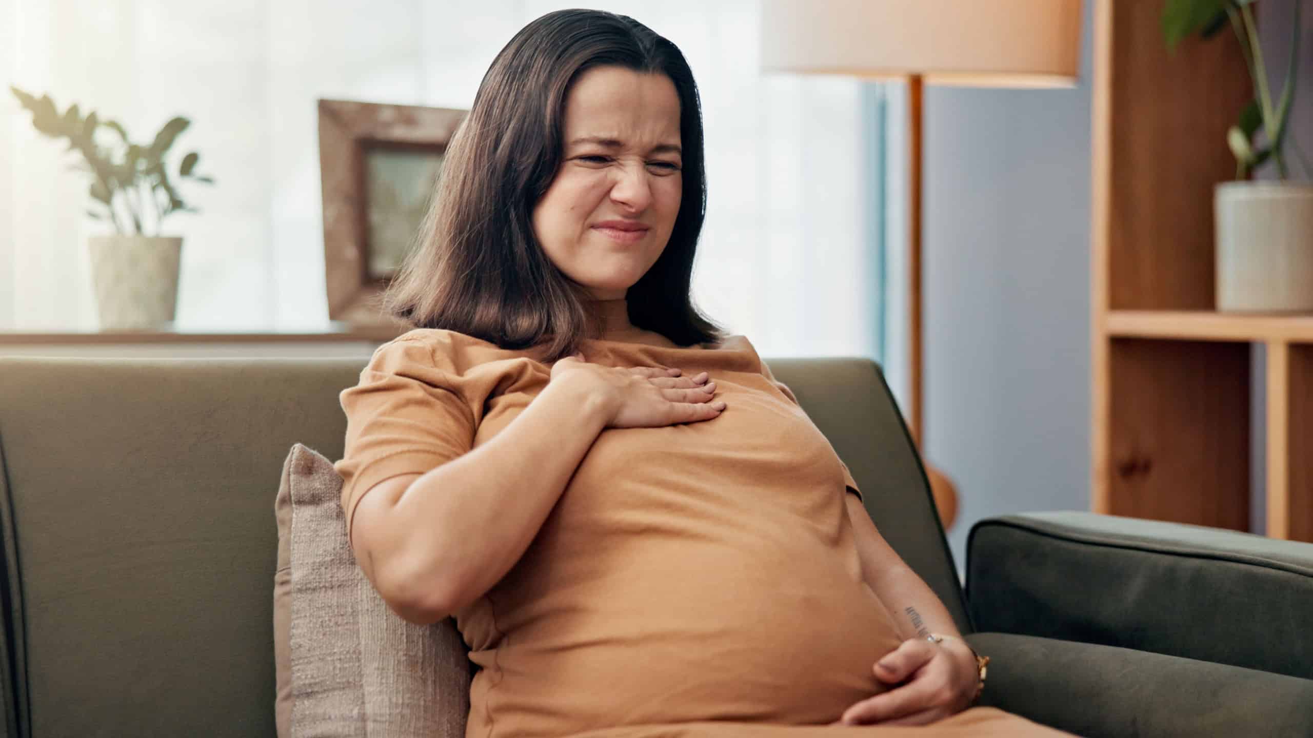Pregnant, heartburn and woman with pain in home for hormonal symptoms, nausea and maternity discomfort. Pregnancy, person and sore chest on sofa with acid reflux, prenatal bloating and healthcare