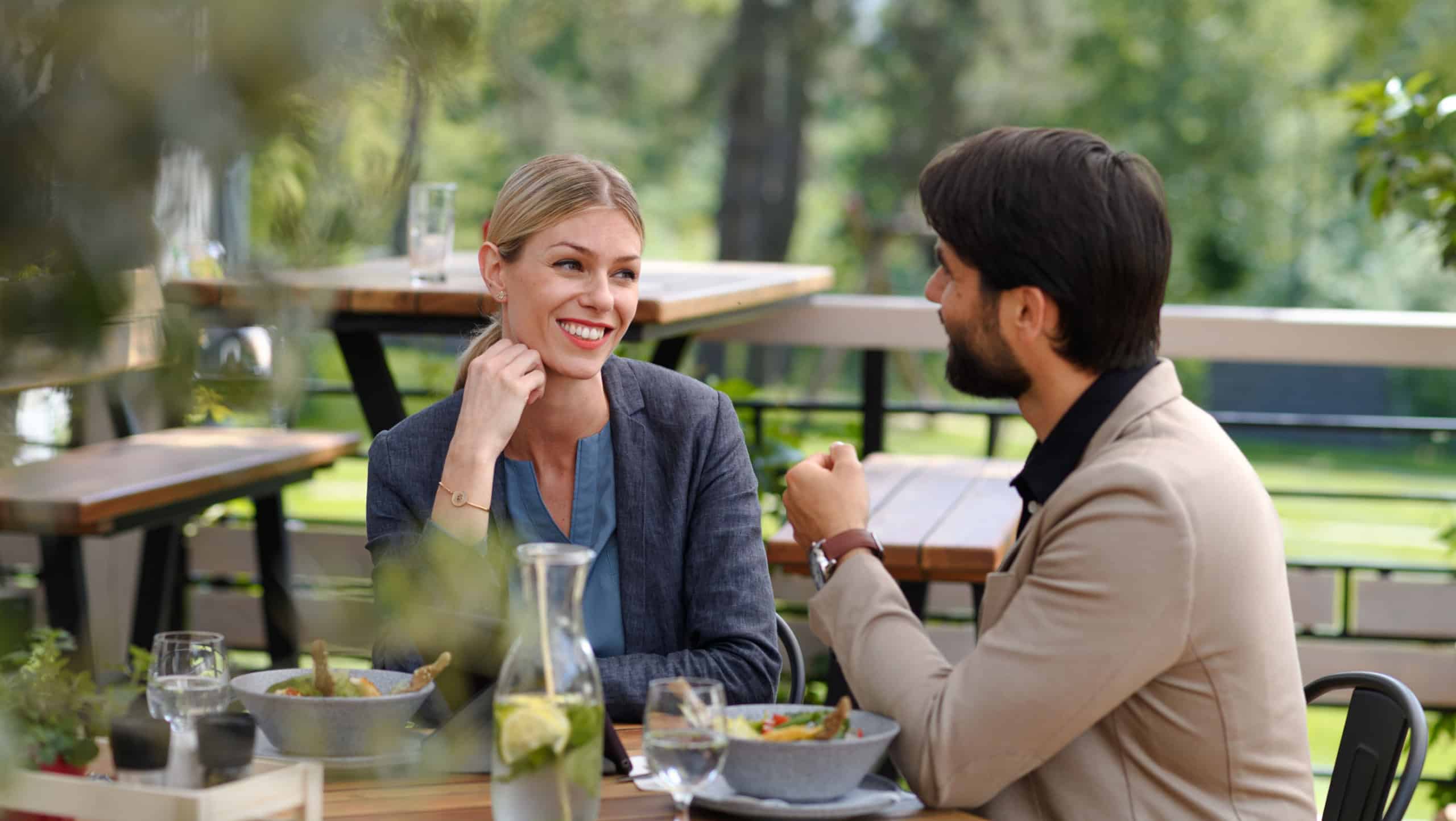 Couple sitting outdoors on terrace restaurant, having dinner date. Business lunch for two managers, discussing new business project.