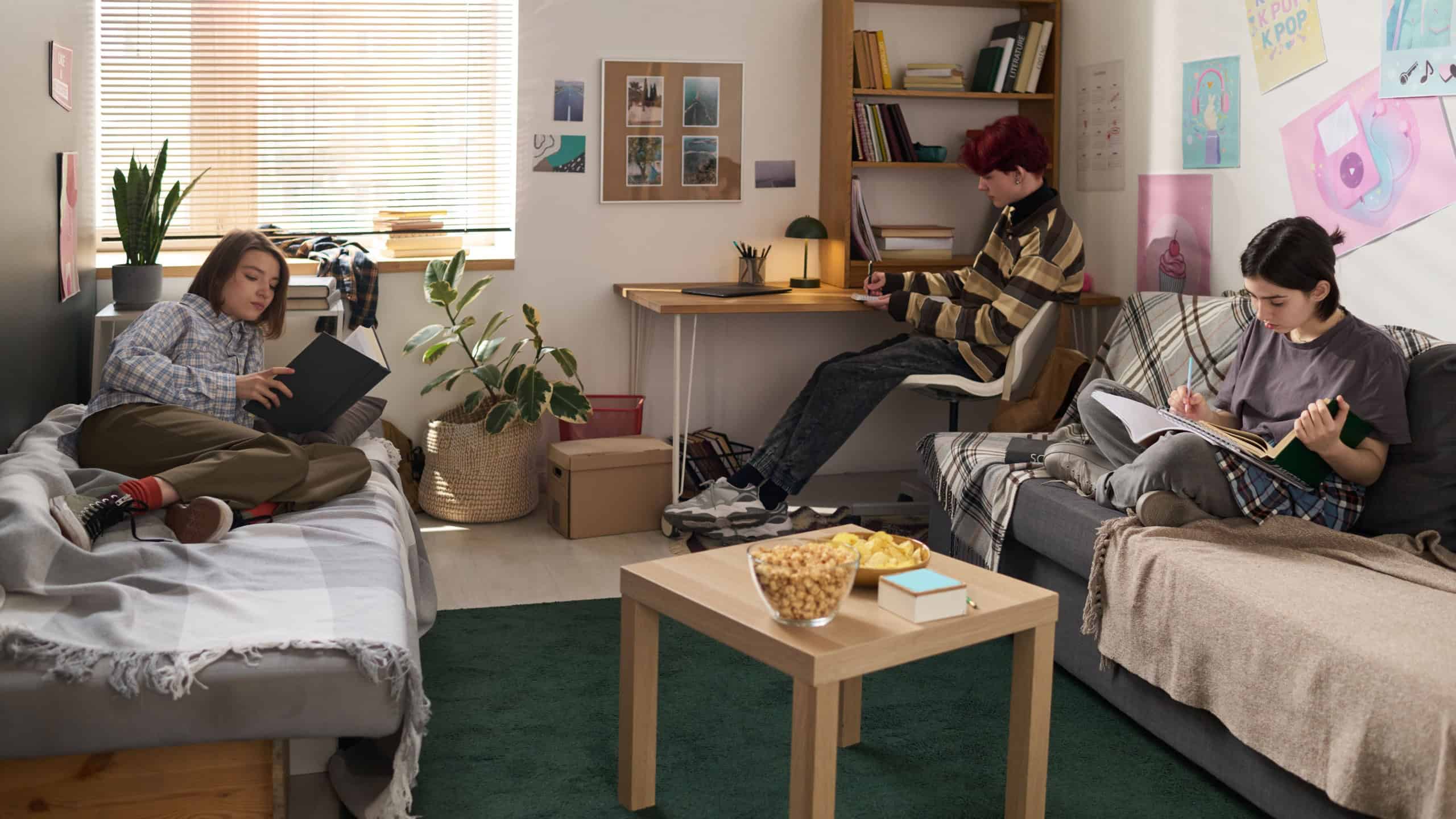 College dorm scene with three teenage friends studying in dorm room with separate activities
