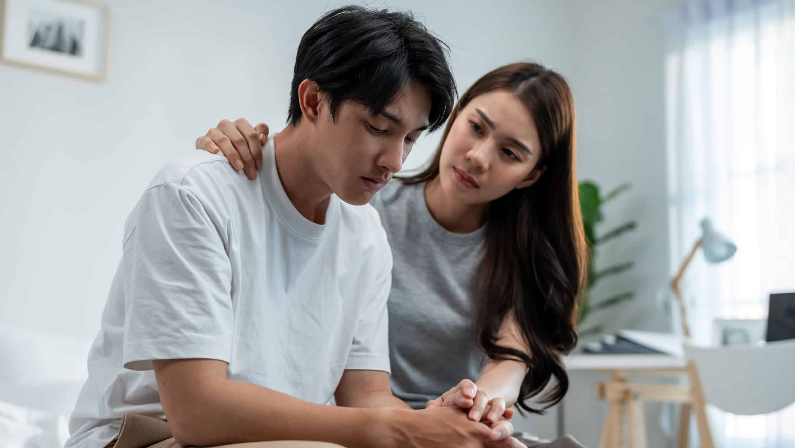 Asian wife comforting her husband crying with tears for life problem. Attractive young woman support, consoling and understand empathy to depressed stressed man in bedroom at home. Family relationship