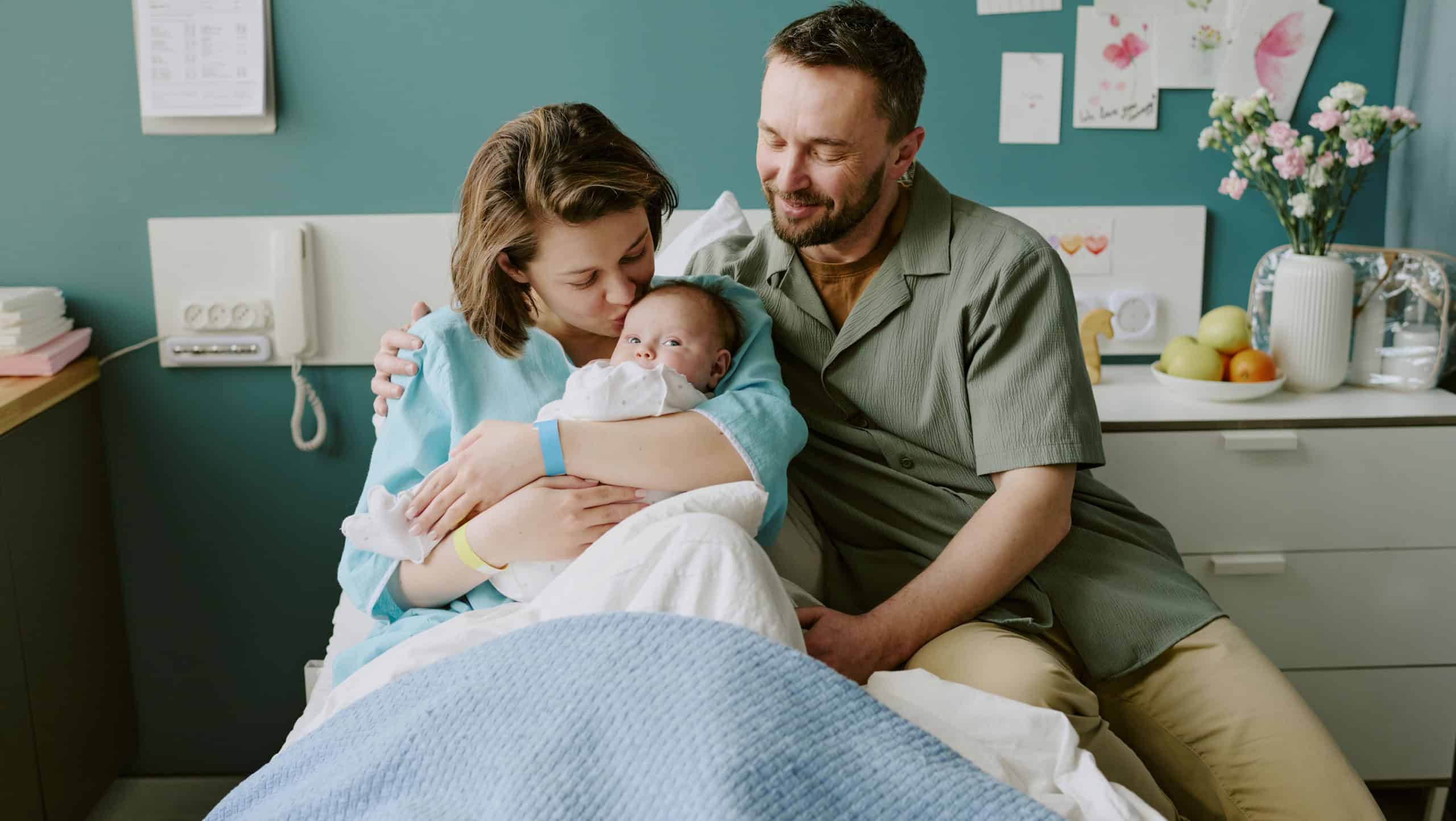 Young parents holding newborn baby in hospital room, smiling and bonding as a family. Caring mother and proud father sharing tender moment