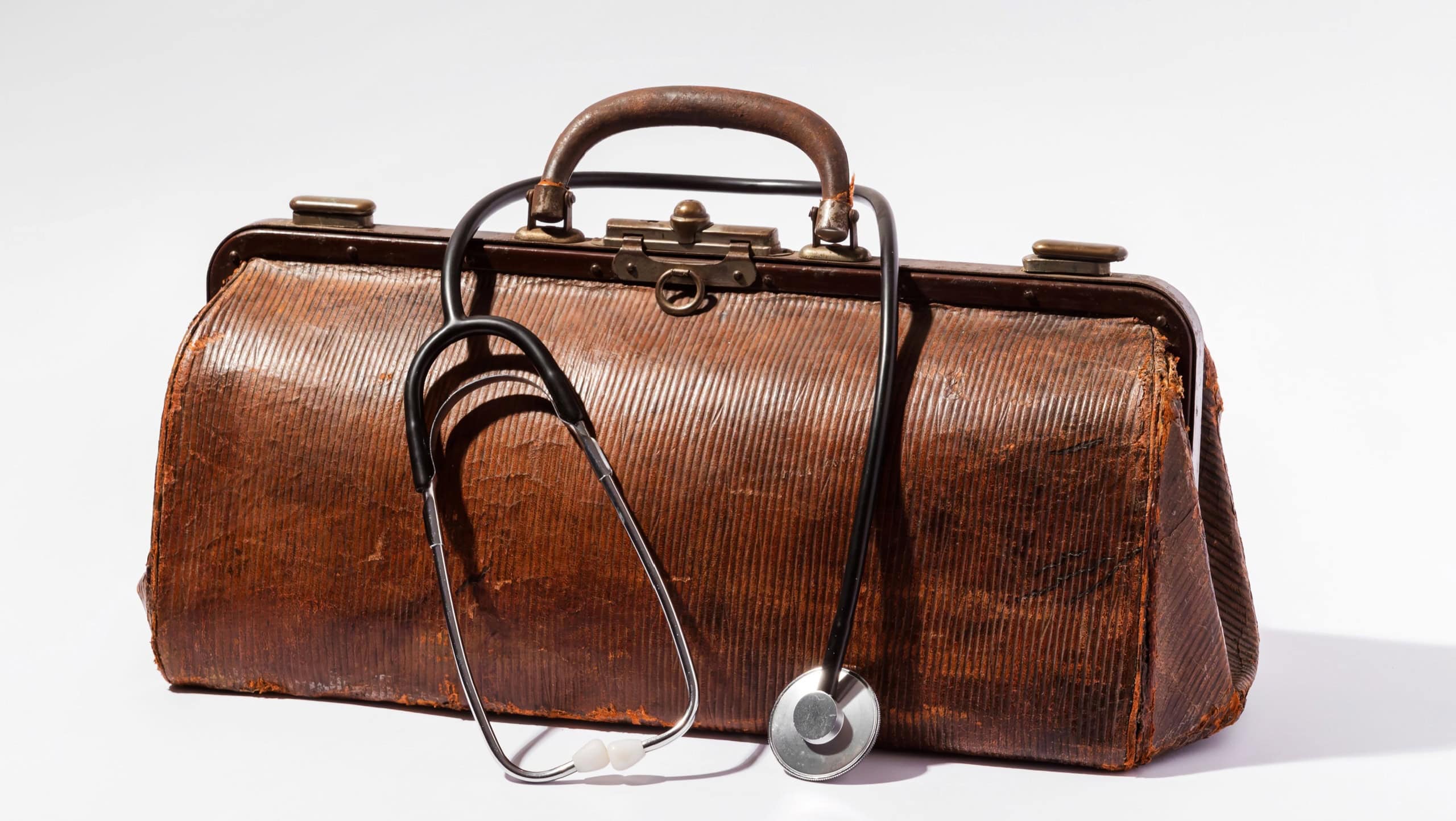Old brown leather doctor bag with stethoscope on white background, representing healthcare and medical history