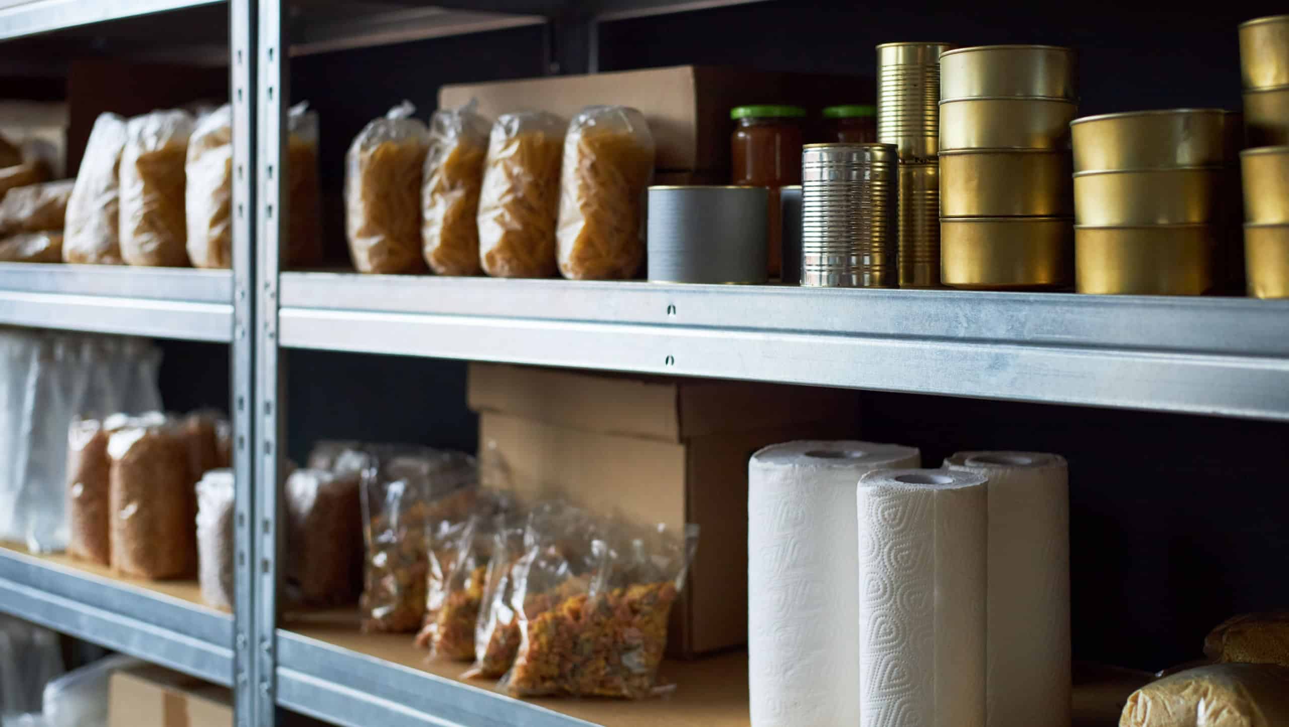 Neatly arranged shelves in well-stocked storeroom showing multiple supplies like canned food, pasta, paper towels, and jars prominently displayed in packages on metal racks