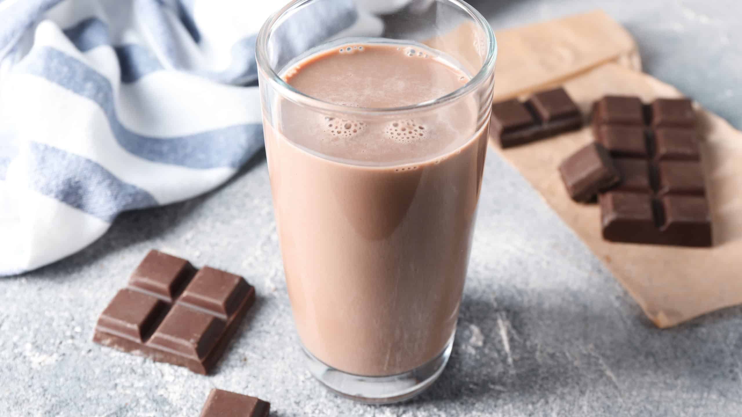 Tasty chocolate milk in glass and pieces on grey table, closeup