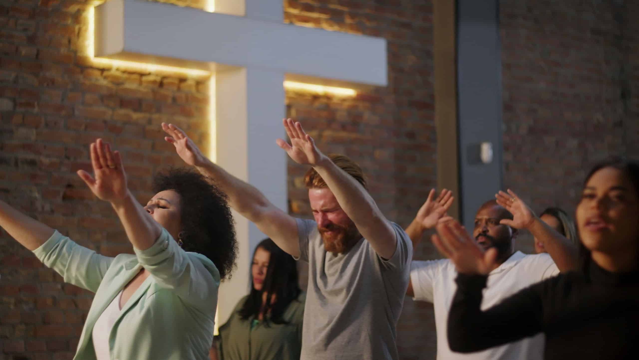 Worship group with diverse individuals raising hands in prayer, eyes closed, emotional expressions, Christian faith community, spirituality, unity in worship, church setting