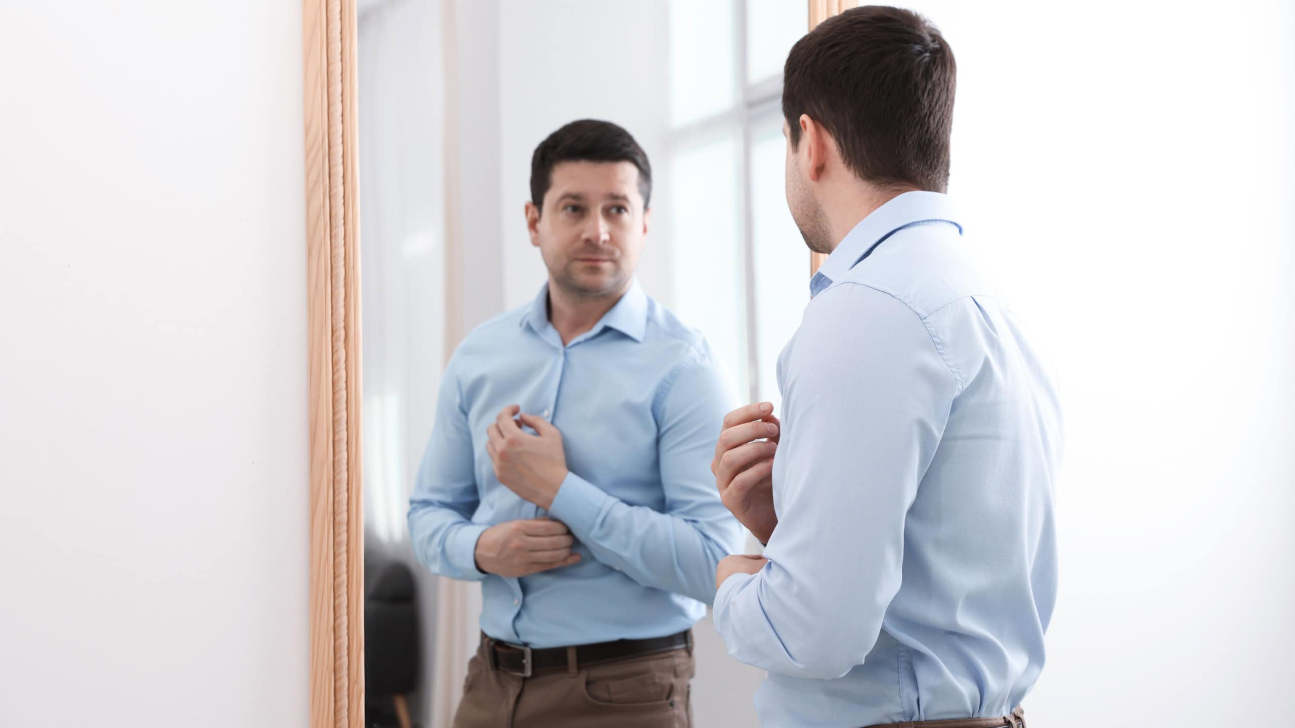 Handsome man looking at himself in mirror indoors