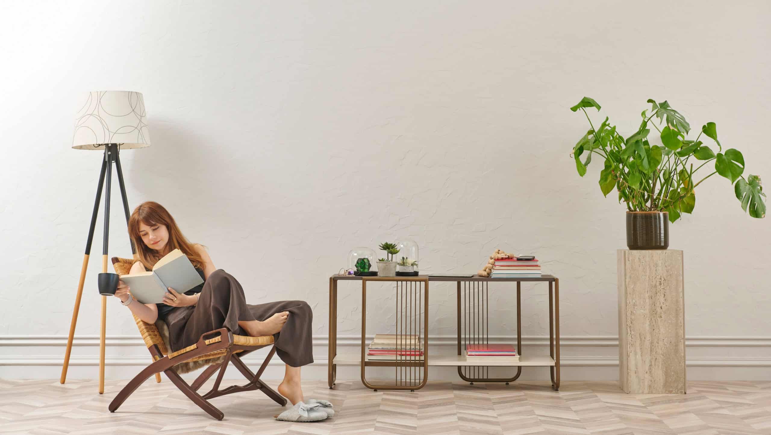 A woman is reading a book at home, looking at the phone and tablet. Decorative interior style and vase of plant.