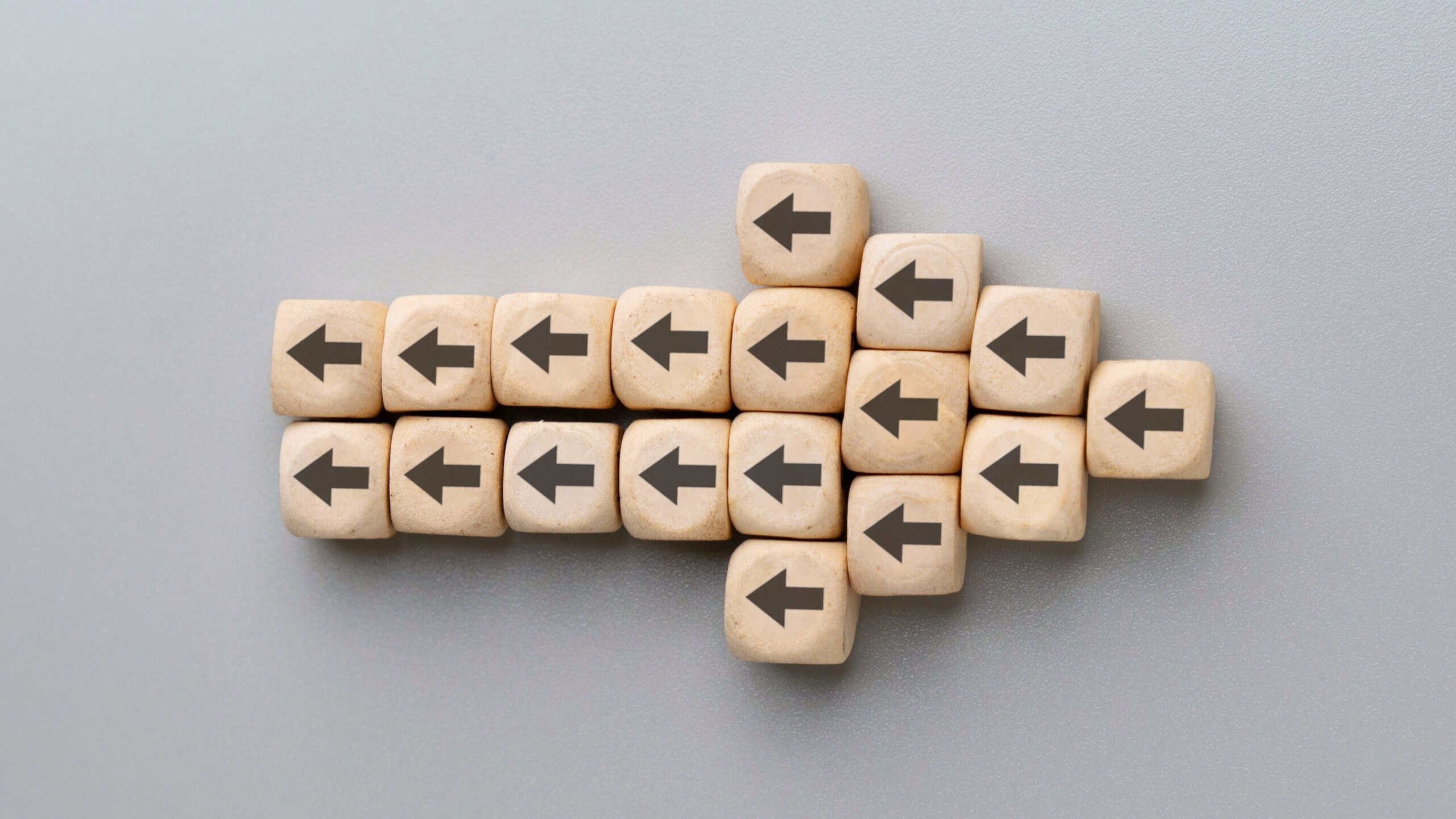 A large arrow formed by multiple wooden blocks with black arrows pointing in the opposite direction. Resistance to change, conflicting directions, stubbornness concept.