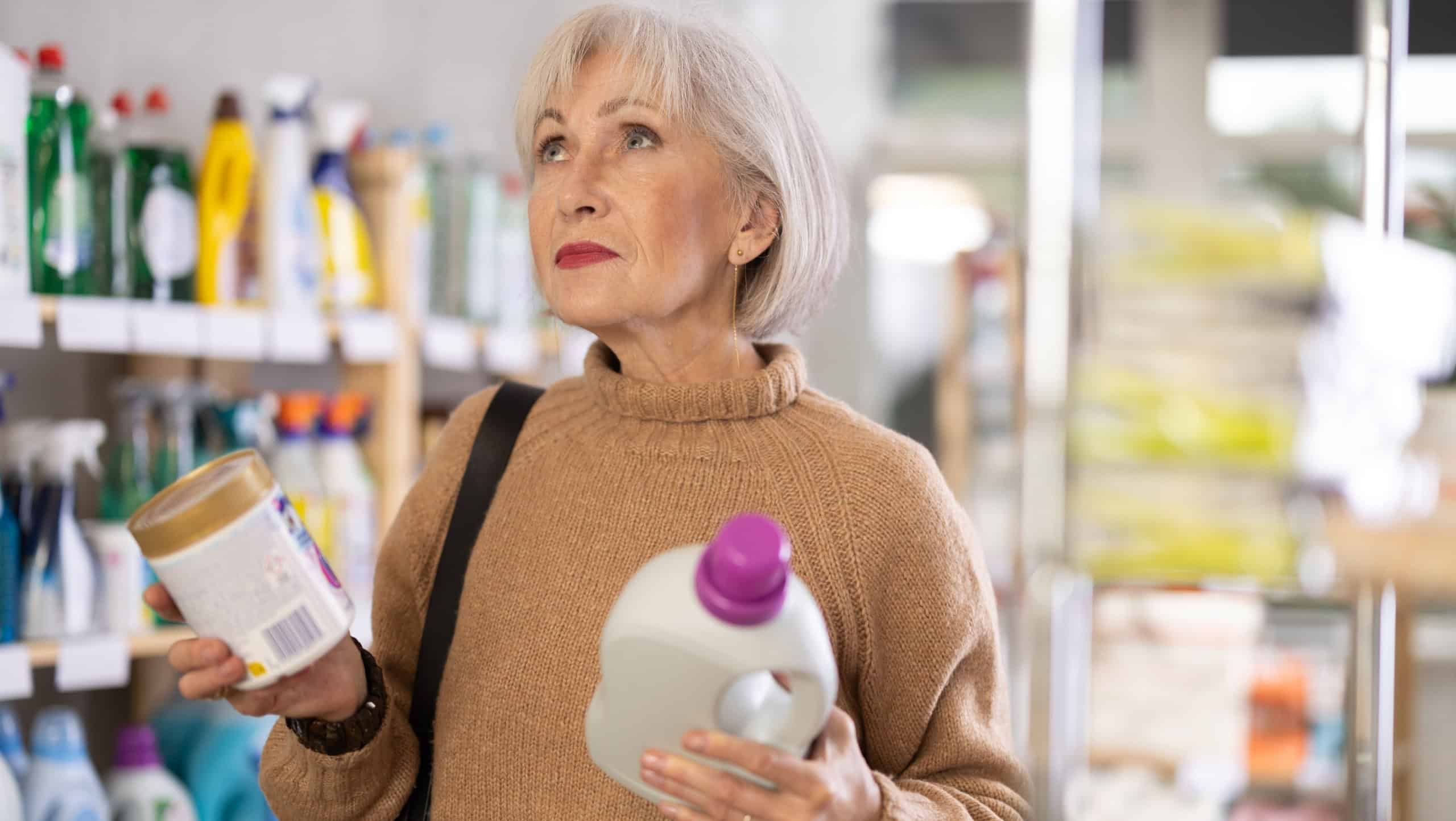 Elderly positive woman consumer with household chemical products for washing indoors