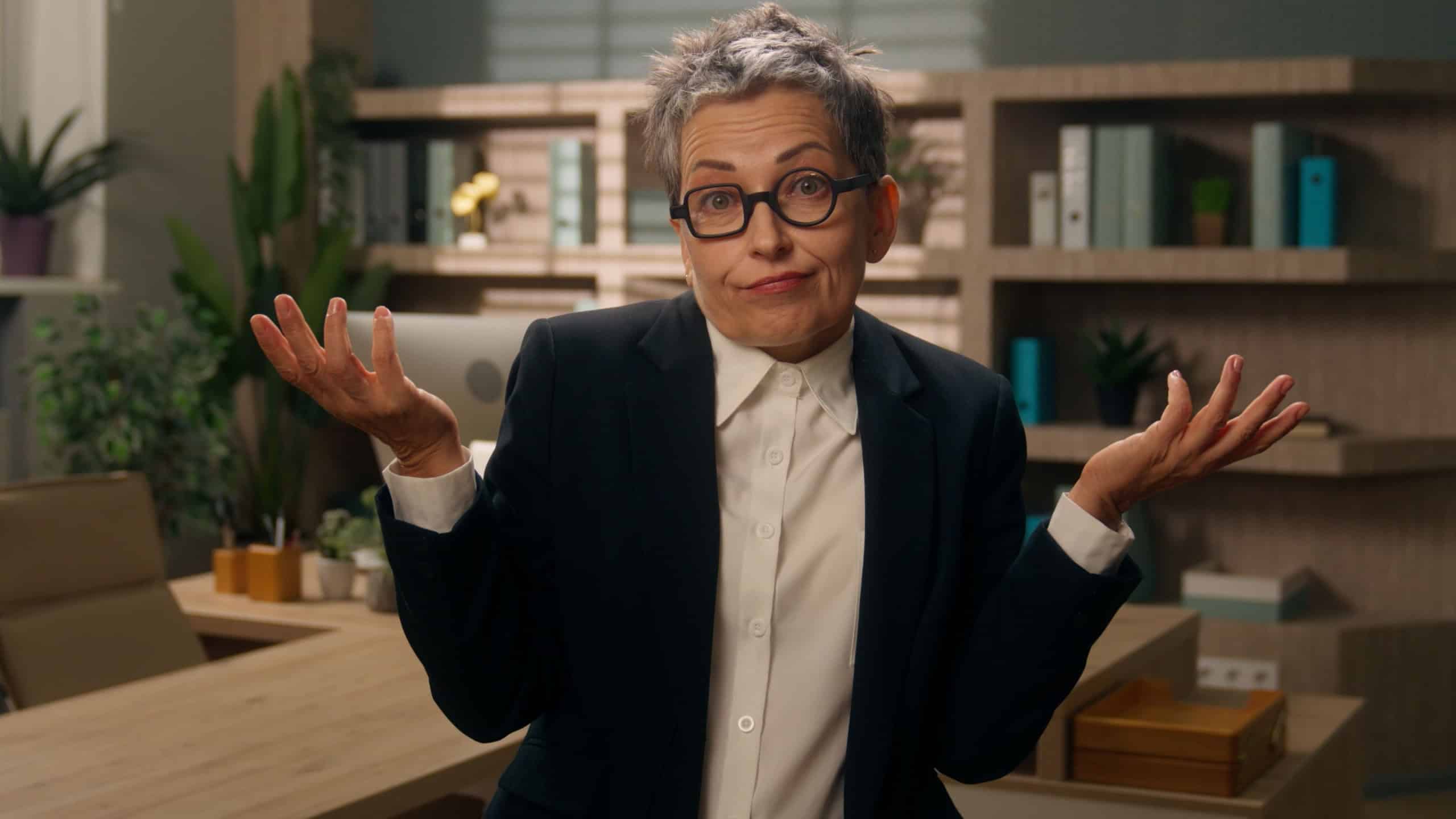 Caucasian business woman senior businesswoman shrug shoulders unsure spread hands confused in office mature female worker retired old employer looking at camera hesitate doubtful reaction uncertainly