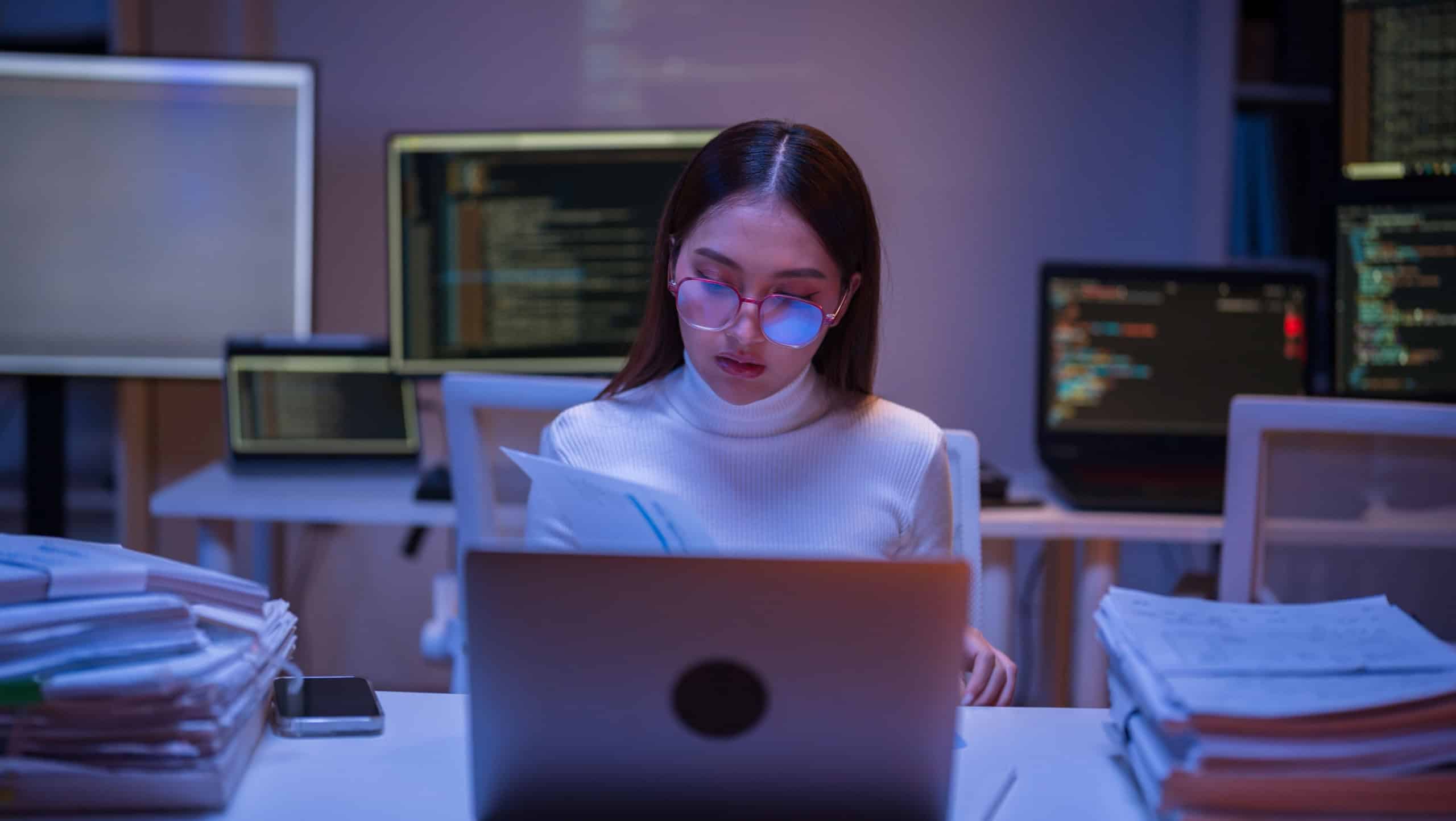 Asian woman working late at night with busy paperwork piled up on her desk, stressed out from not being able to finish her work in the office