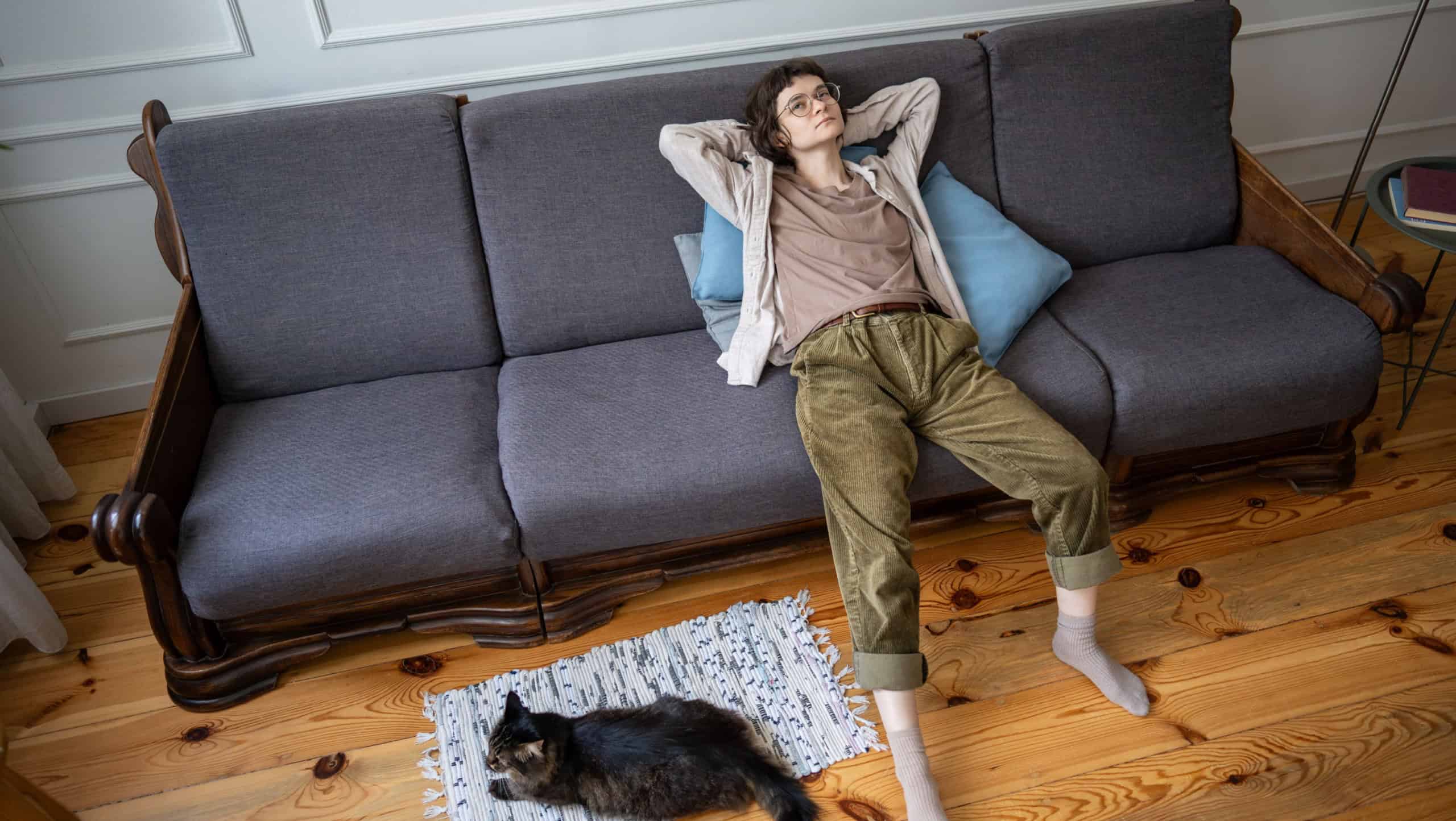 Tired lazy young woman lying on sofa and looking up, bored and apathetic female and cat in isolation at home. Loneliness with pet, depression melancholy, indifferent life, slow living of pet owner