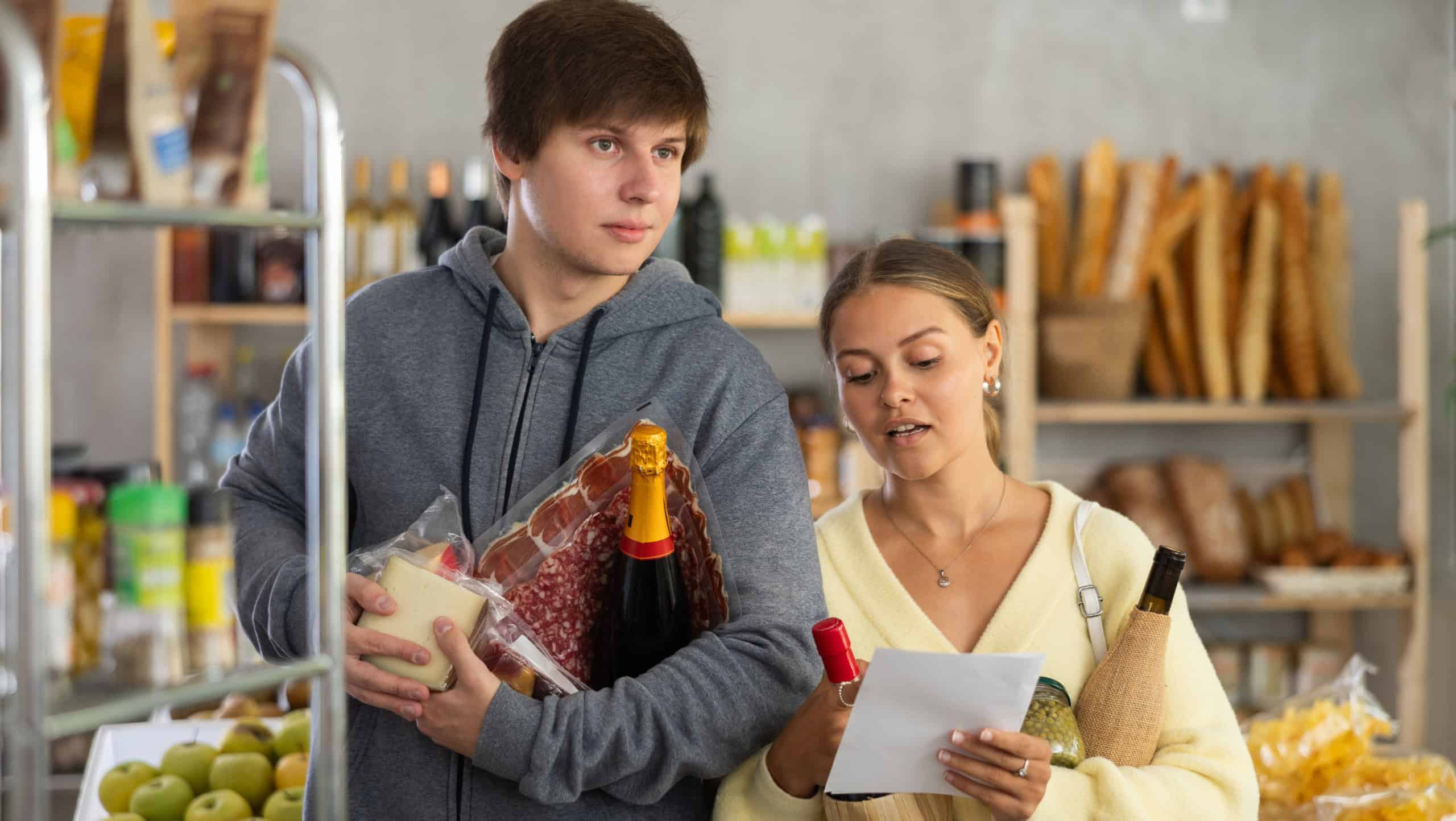Young couple shopping together, choosing items from a pre-made list at a grocery store