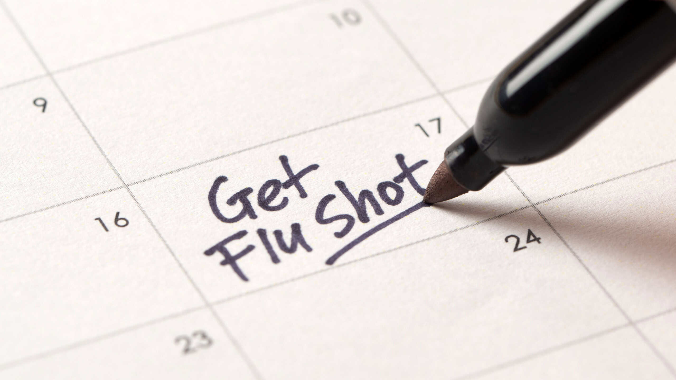 A close-up of a calendar with a handwritten note saying Get Flu Shot, serving as a reminder for an important health appointment. A symbol of influenza prevention and personal healthcare planning