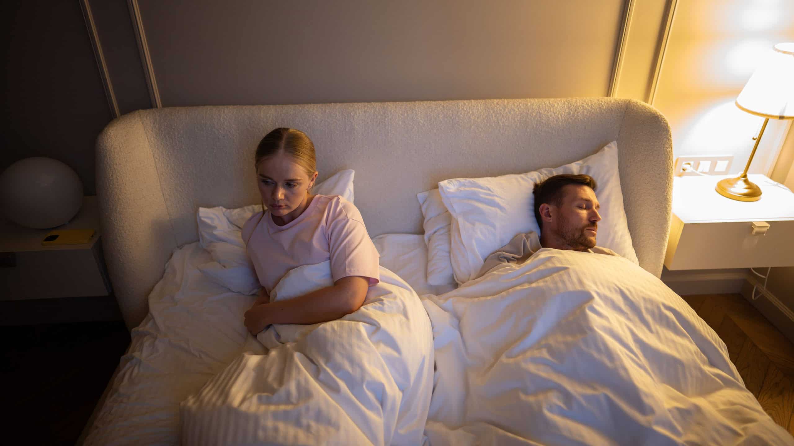 Exhausted wife unable to sleep at night from partner loud breathing in room. Sleep disruption, chronic fatigue in marriage, night insomnia, emotional strain from snore, lack of rest in relationship