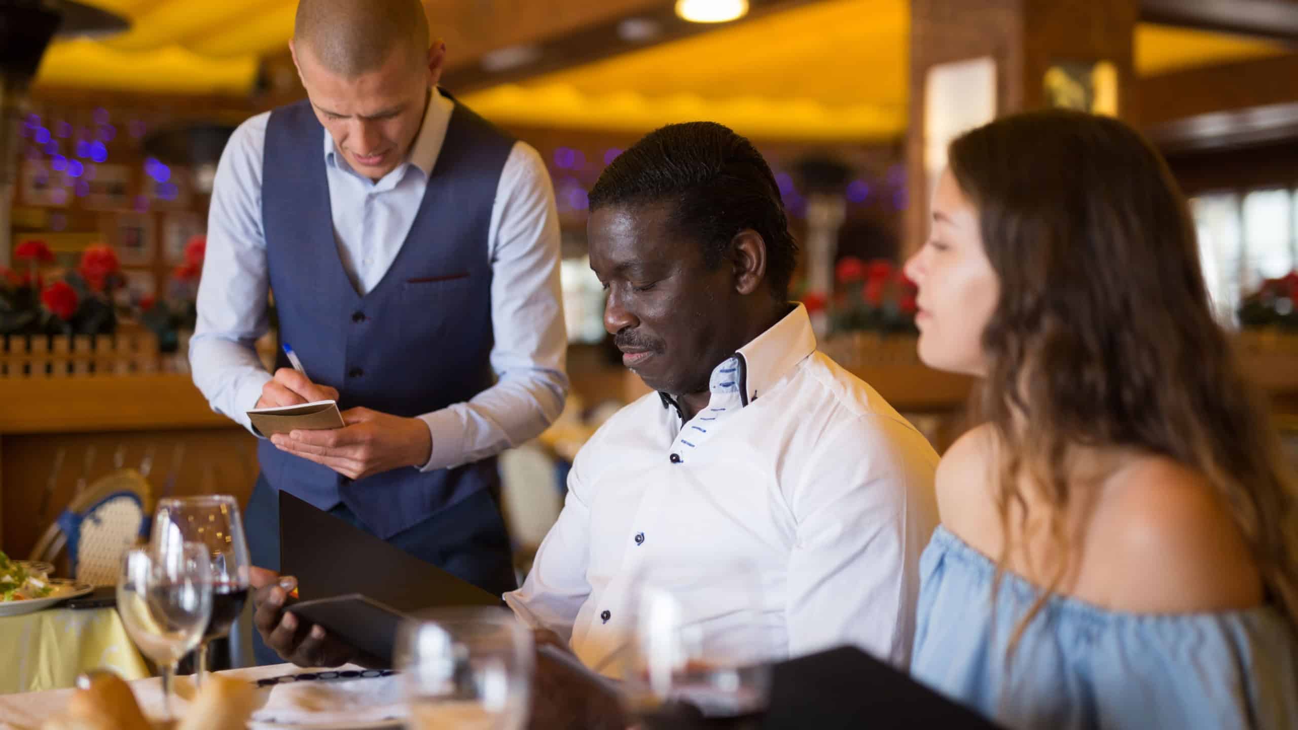 Couple looking in menu, talking with waiter and making order at restaurant
