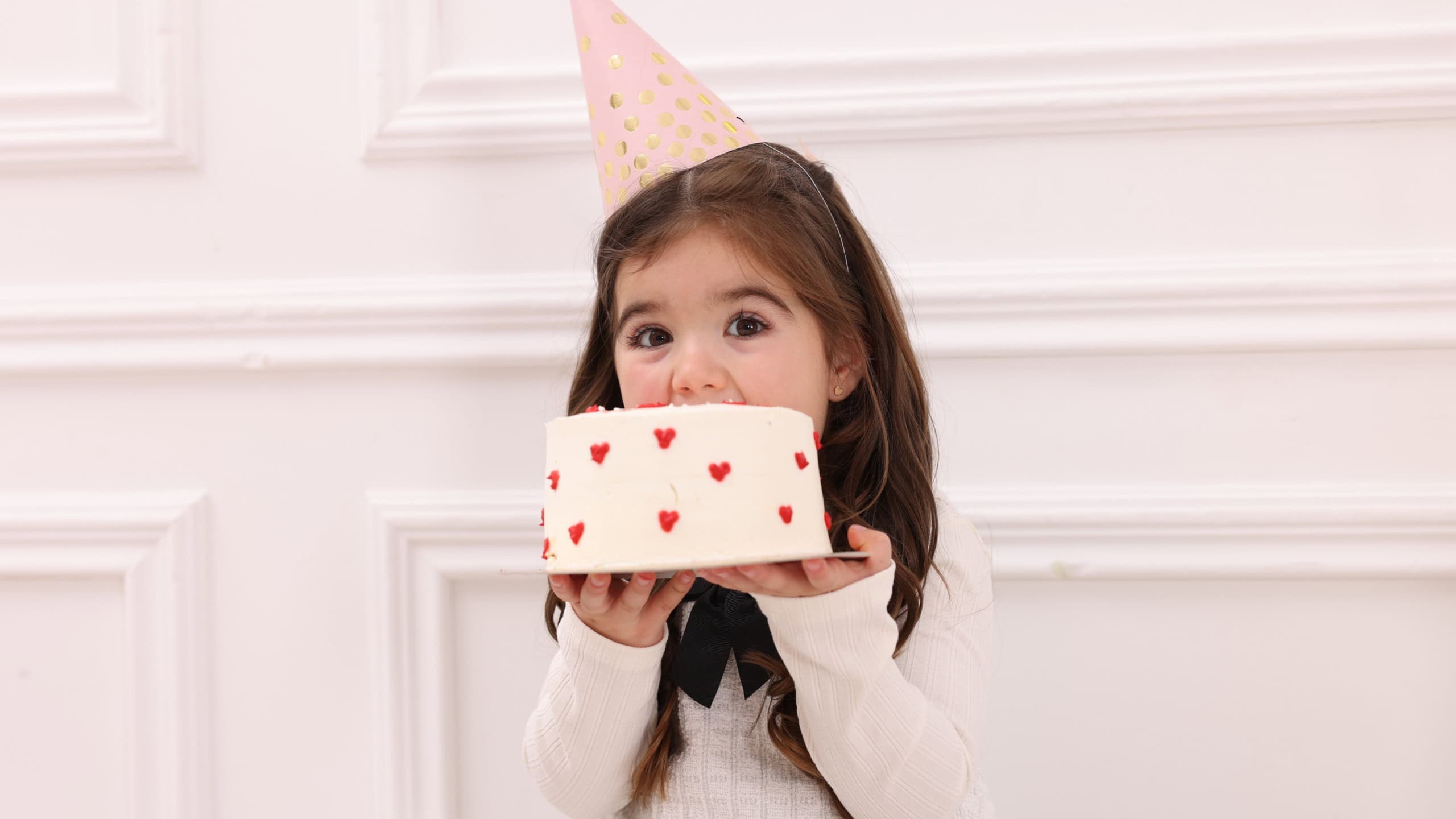 Birthday celebration. Cute little girl in party hat eating tasty cake indoors