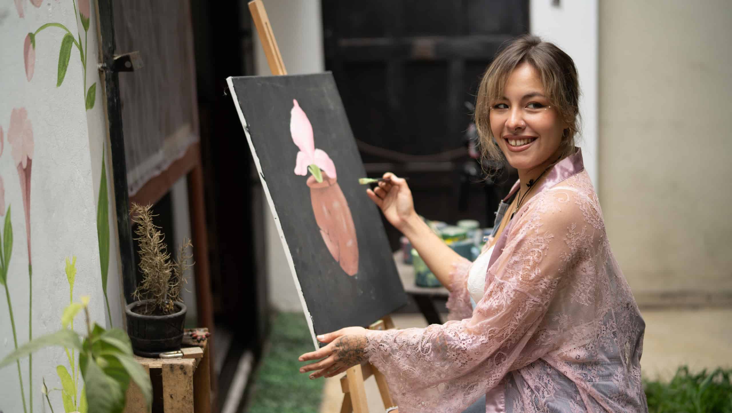 Smiling woman artist painting on canvas outdoors at an easel, expressing creativity, passion and relaxed concentration in daylight