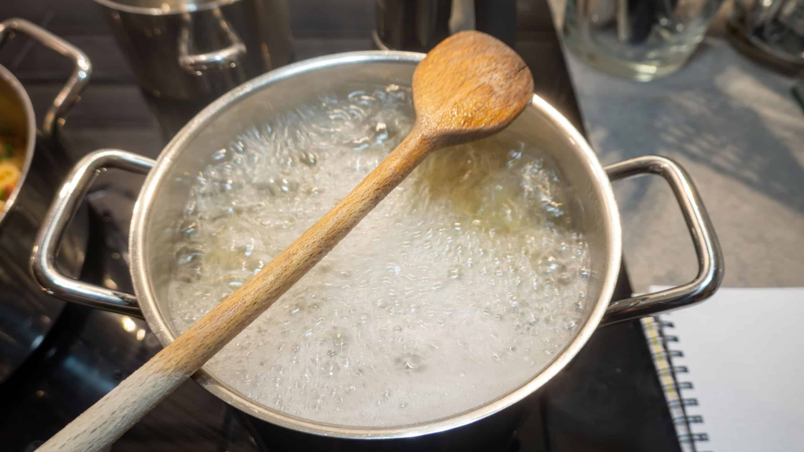 Pasta boils in a pot of water and a wooden spoon to prevent overflow.