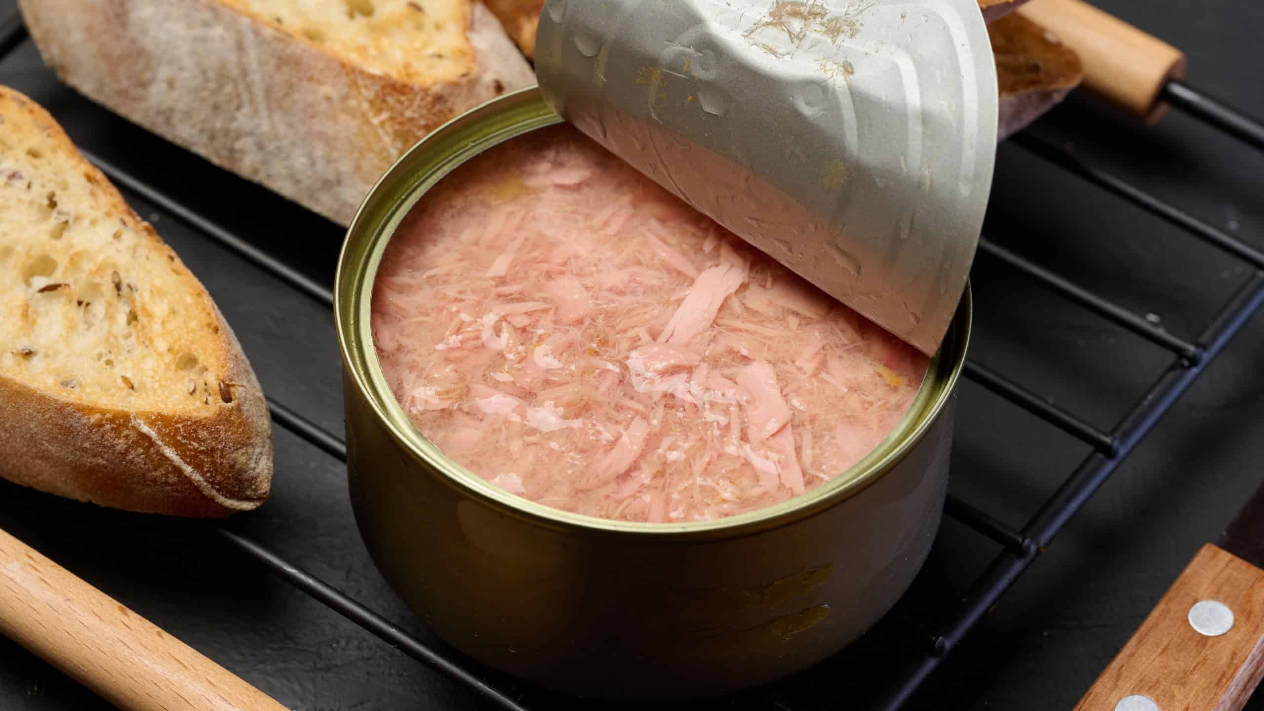 An open tin can of tuna and slices of bread