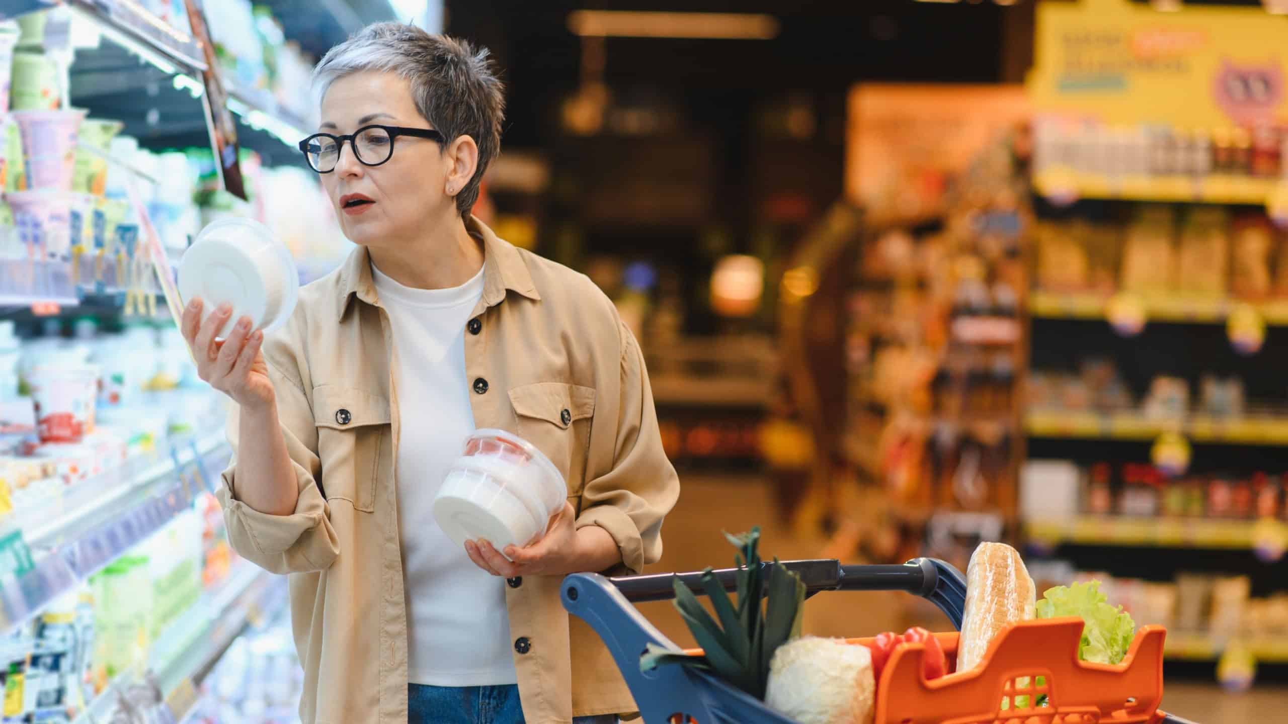 Woman standing in a grocery store aisle, comparing product labels and making informed decisions about healthy food items for her family