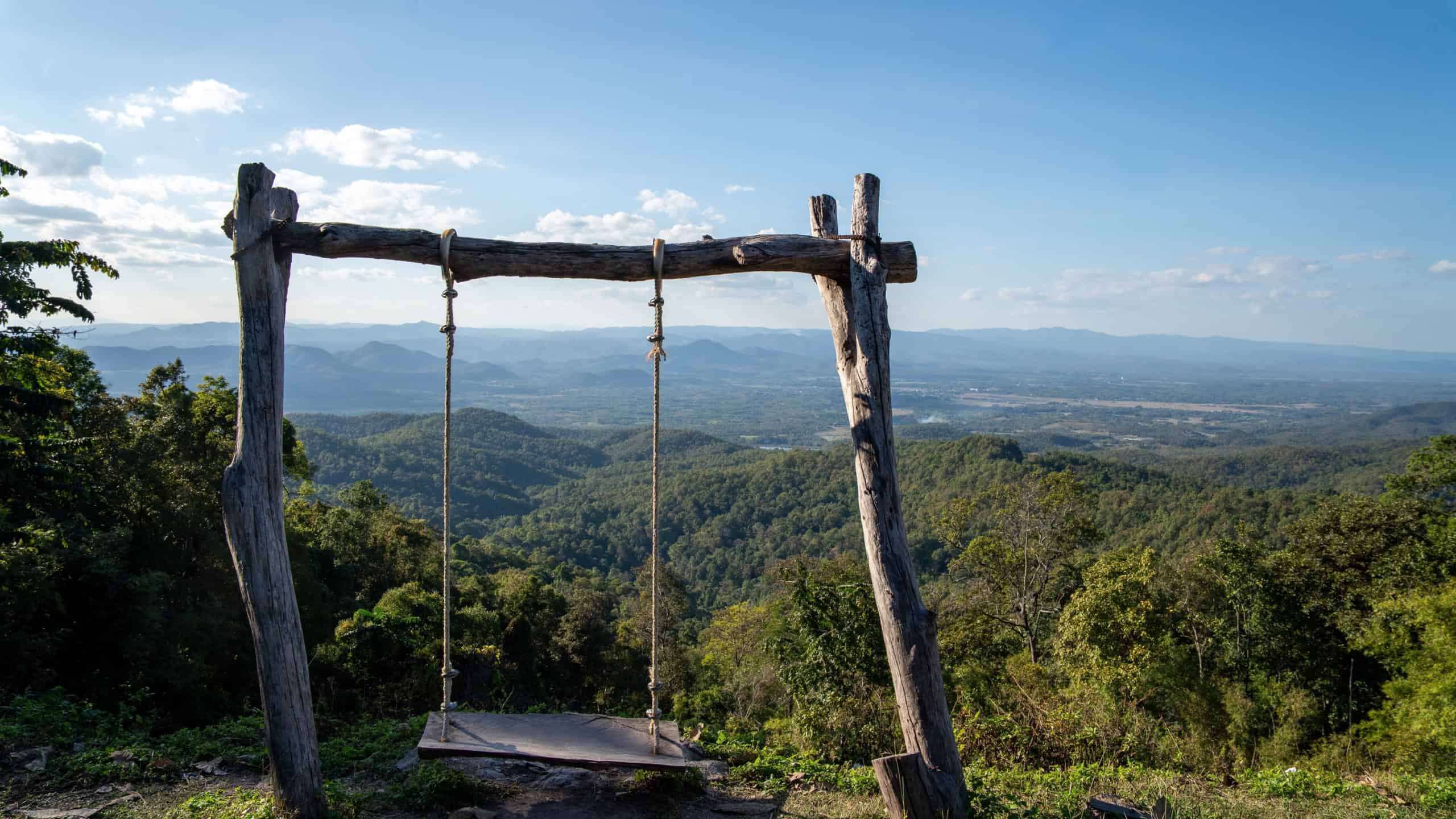 Rustic wooden swing overlooking a vast green mountain landscape under blue sky, scenic viewpoint symbolizing freedom, travel, relaxation and connection with nature.